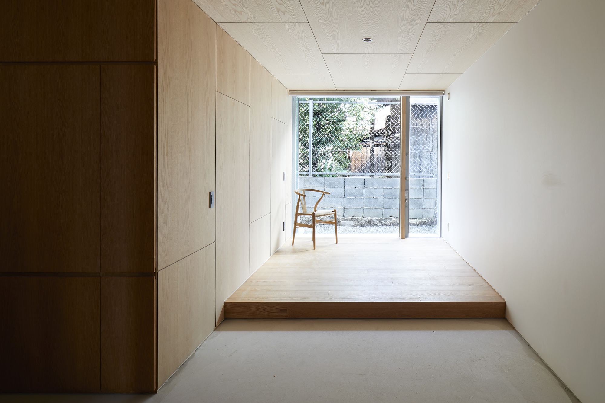 Corridor with pale timber storage wall leading to glazed doors opening onto a mesh-screened courtyard