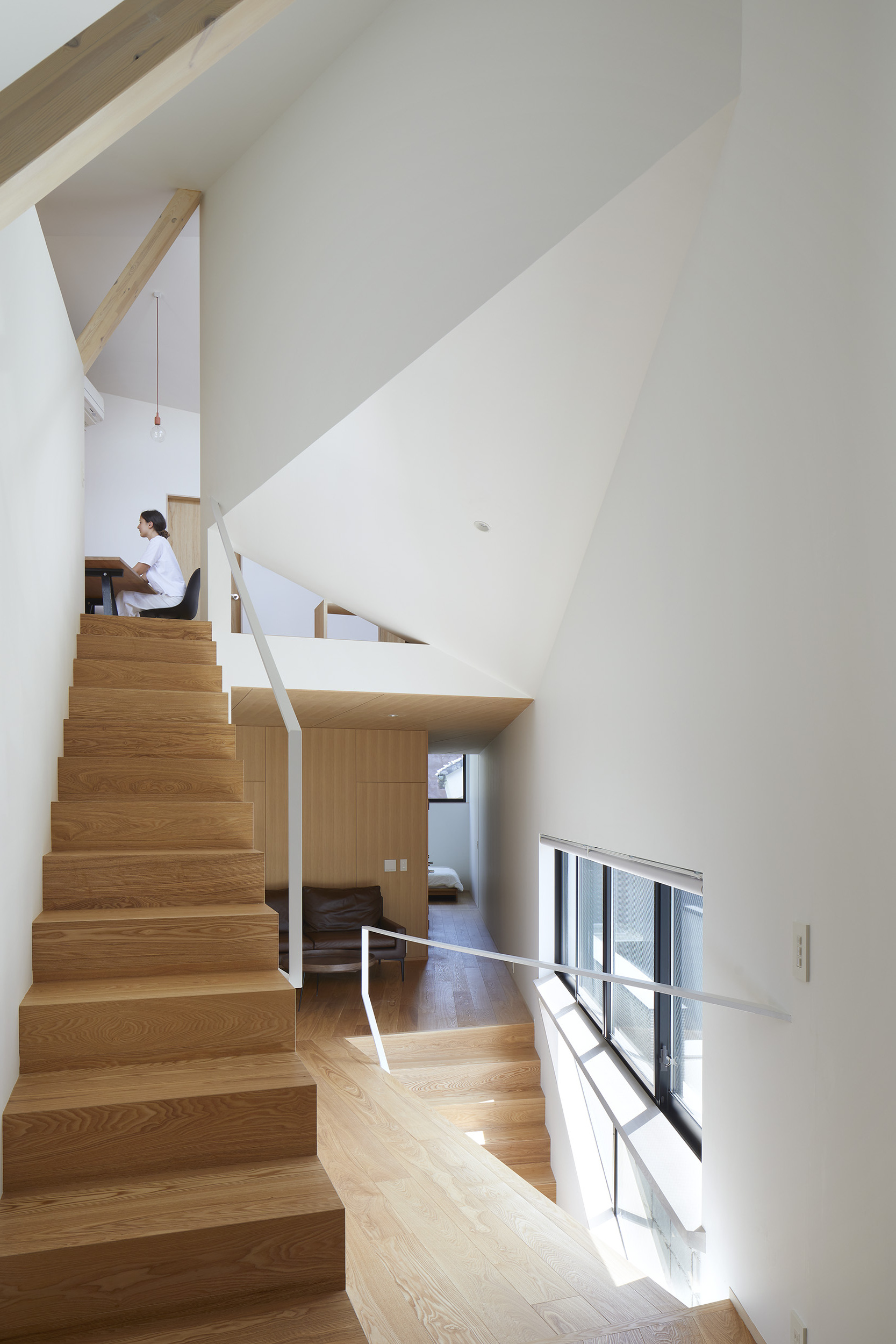 Multi-level interior with timber staircase and white metal railings where a person sits on an upper landing