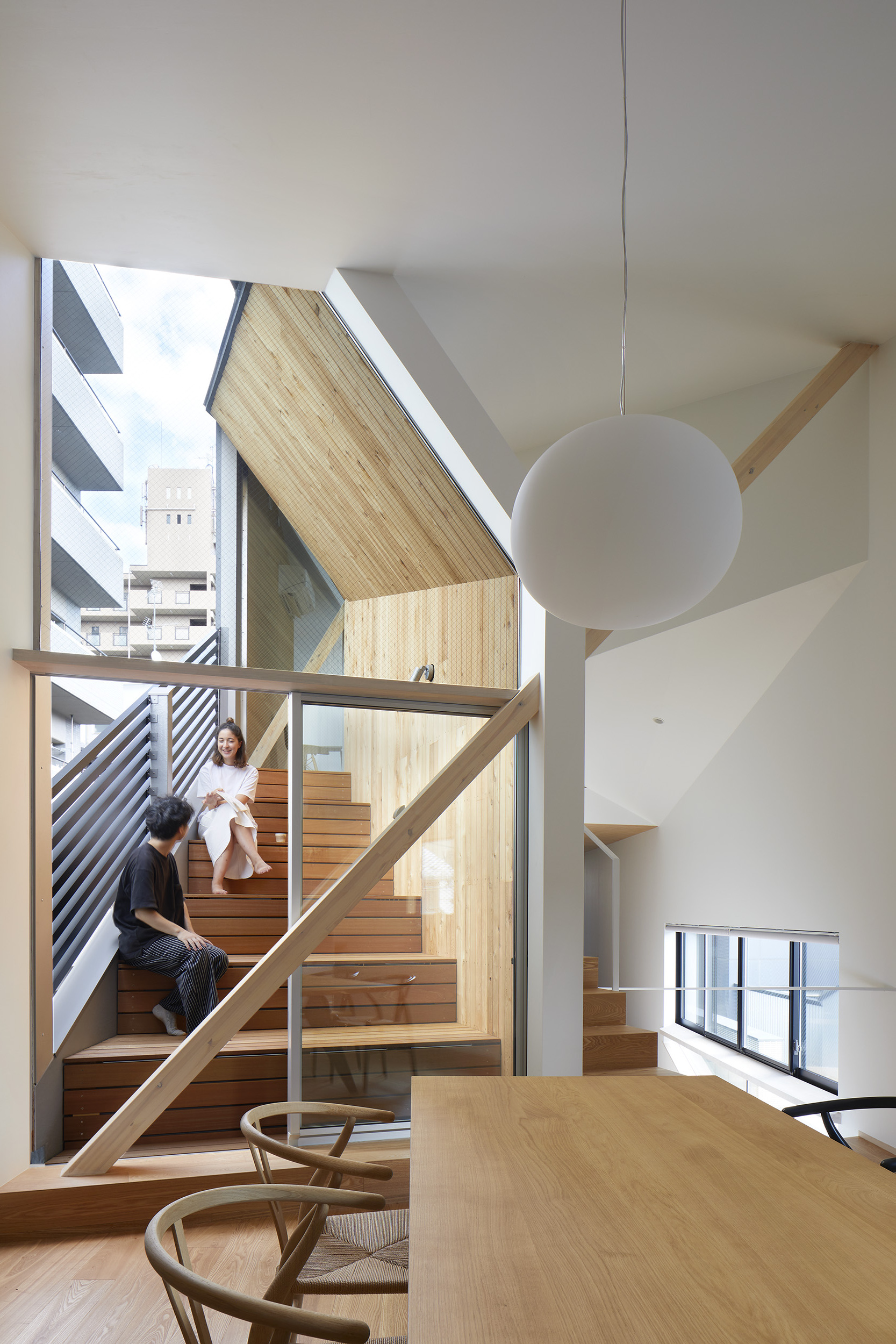 Double-height stairwell with exposed timber beams and large glazed wall overlooking neighboring rooftops