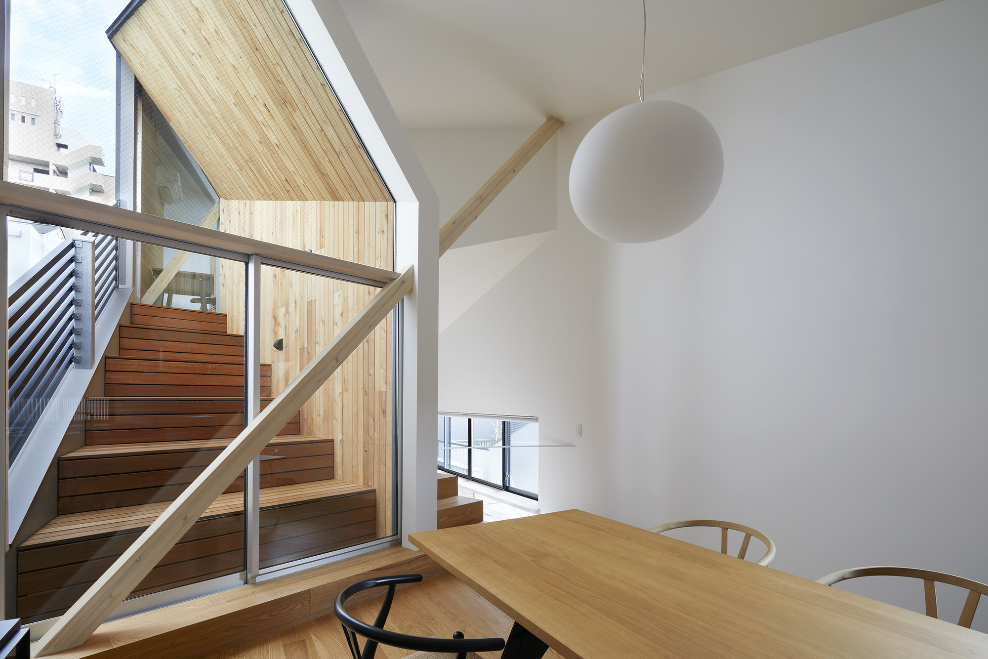 Dining area with timber table and glazed wall opening to external timber stair and metal balcony