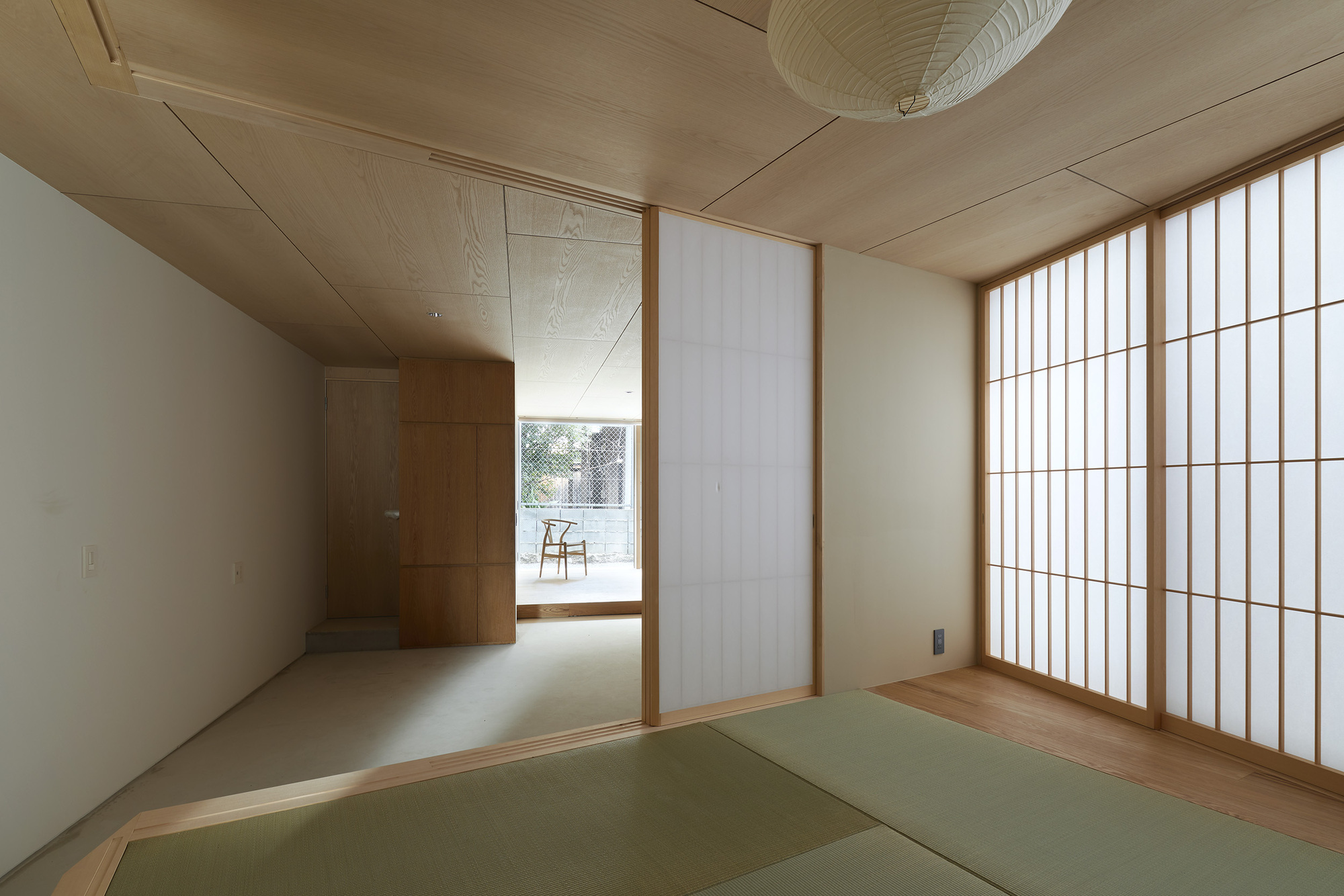 Tatami mat room with translucent shoji screen wall and plywood ceiling with paper pendant light