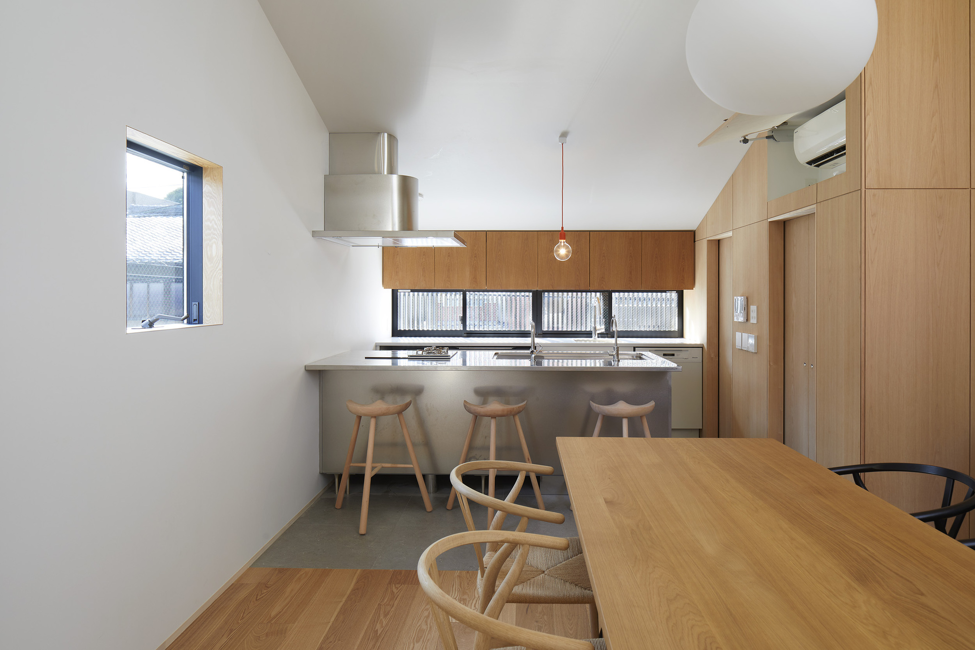 Open kitchen and dining area with timber cabinetry and three wooden stools at the counter