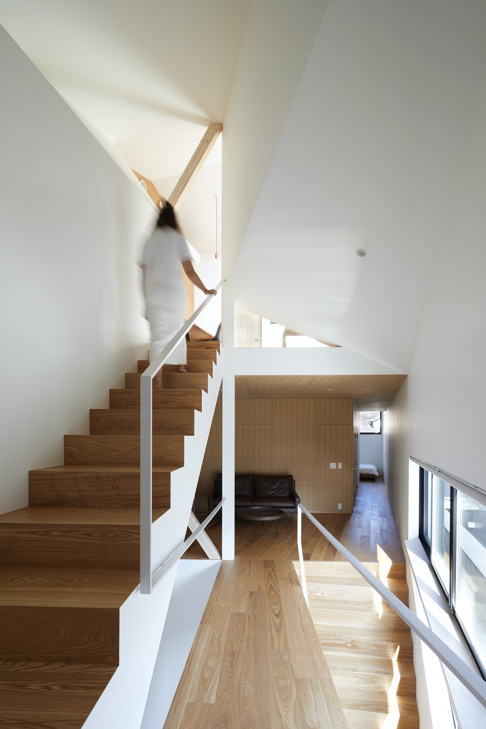 Timber staircase with white metal railing as a figure ascends toward a skylight above