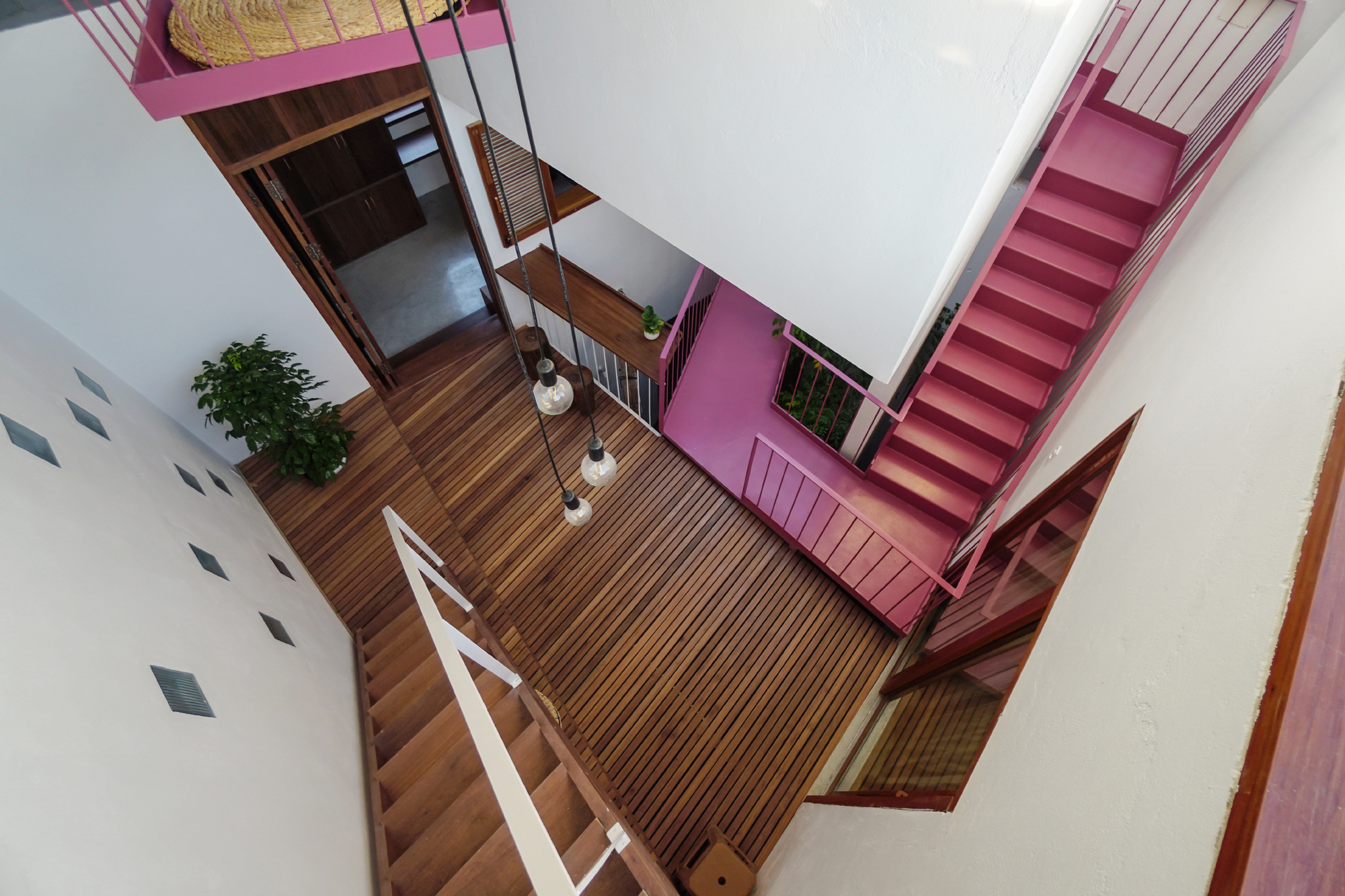 Top-down view of interconnected pink steel staircases around a central void with timber decking