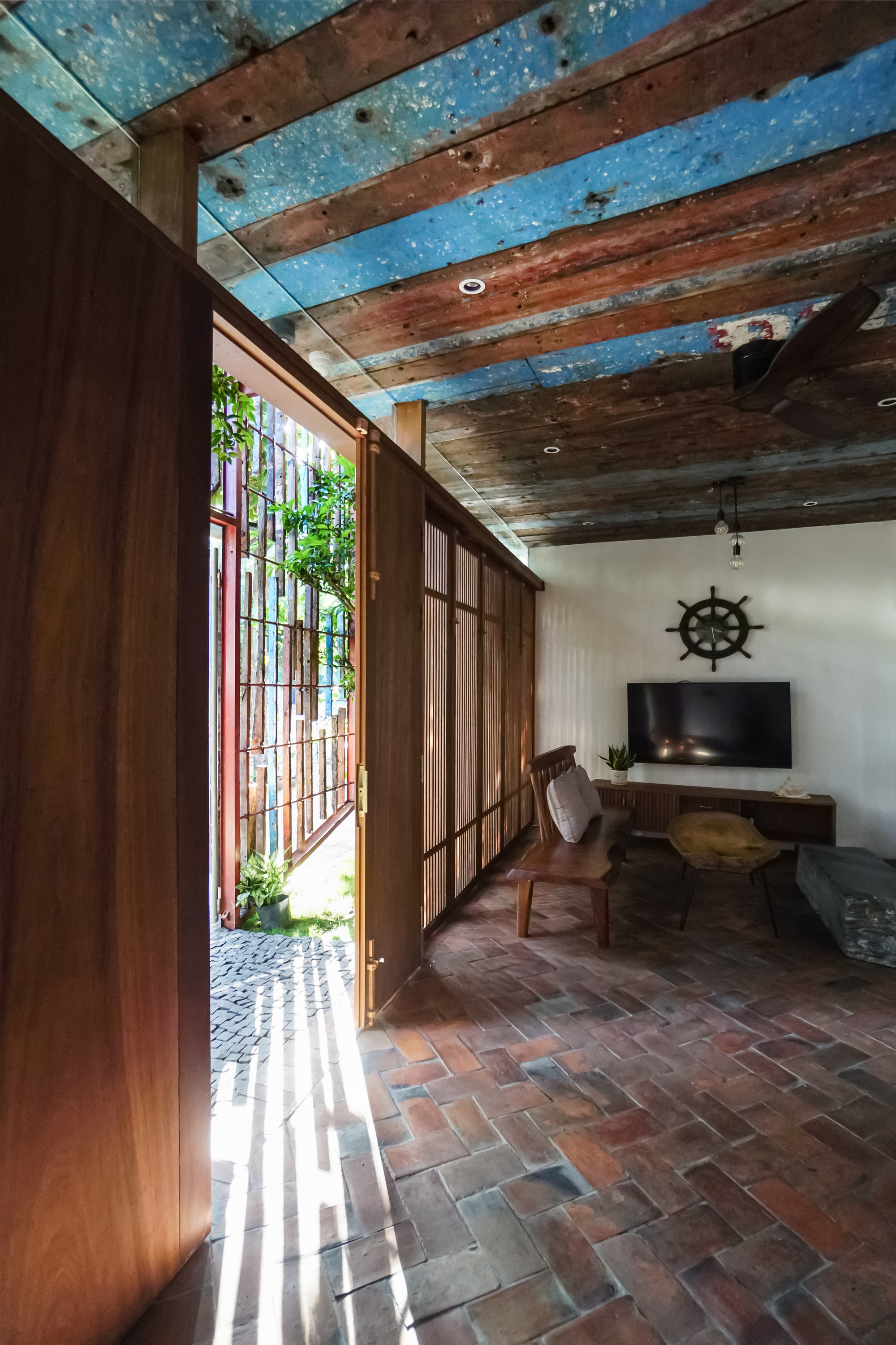 Interior room with reclaimed metal ceiling panels, herringbone brick floor and timber screen opening to garden