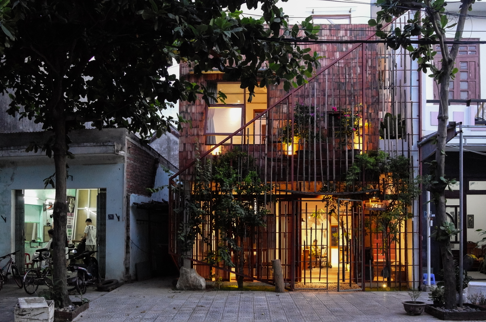 Evening view showing the illuminated interior visible through the metal rod facade and planted terraces