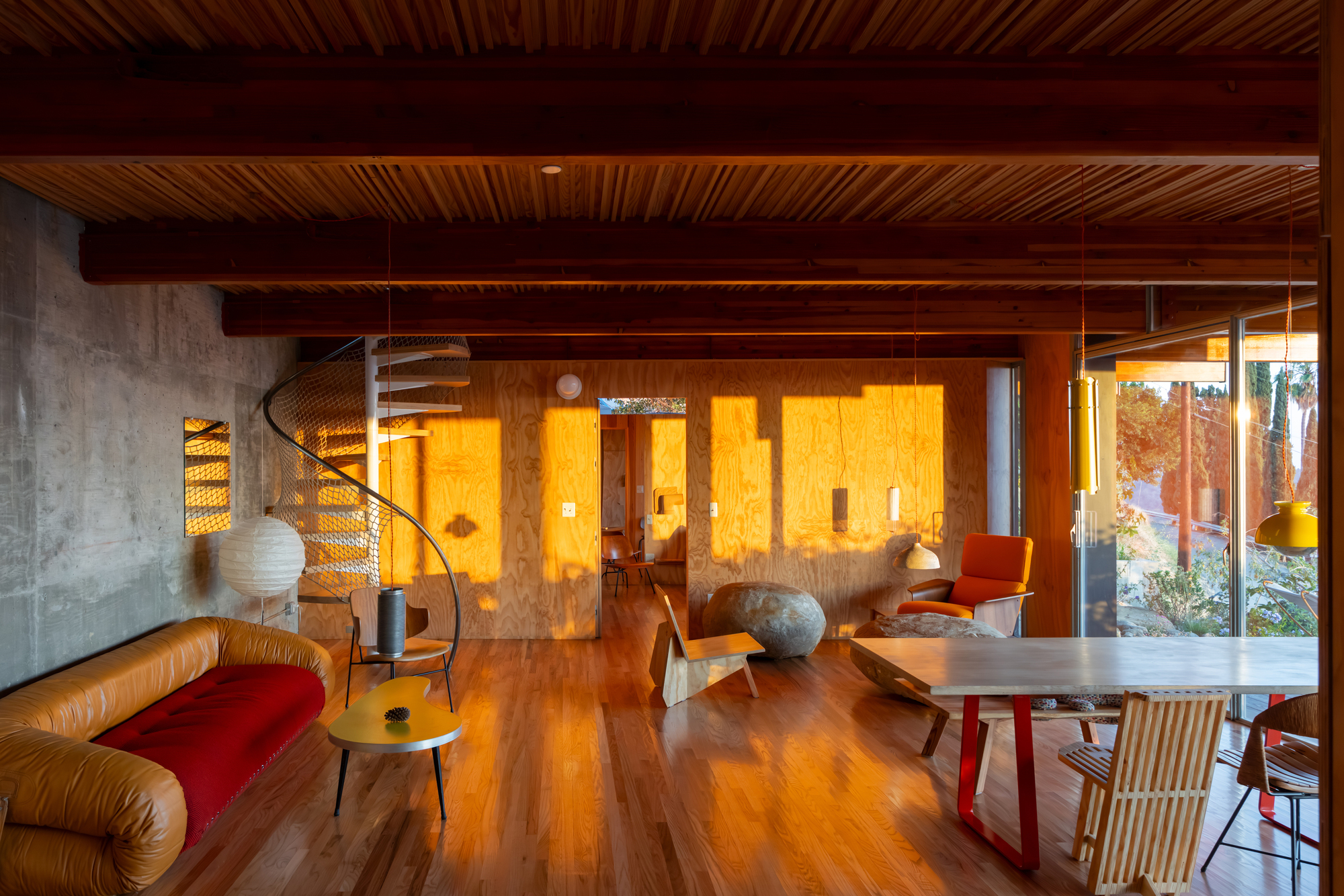 Living area with exposed timber beams and concrete wall beside spiral stair illuminated by warm evening light