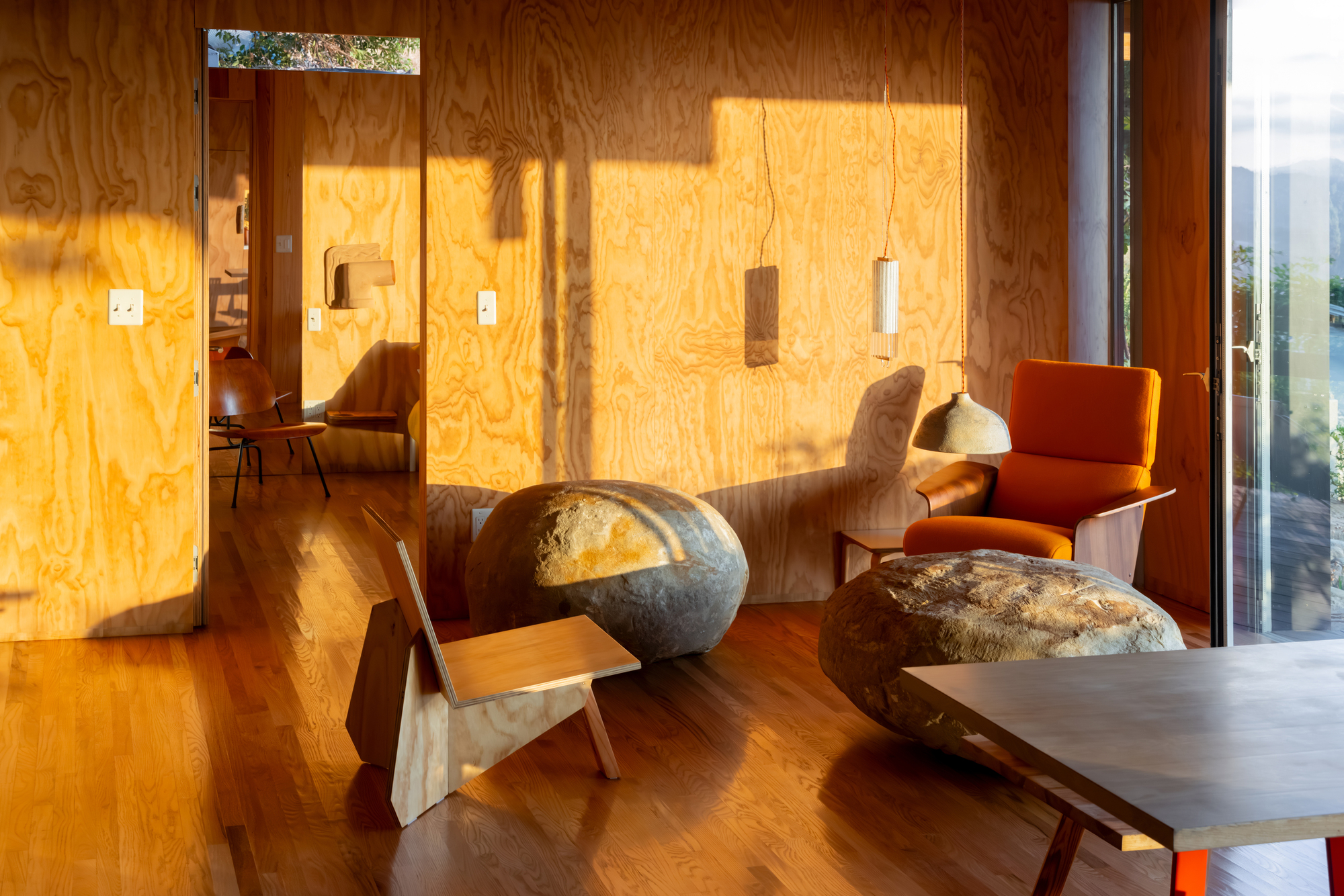 Living room with plywood walls catching afternoon sunlight and a sculptural stone coffee table on wood flooring