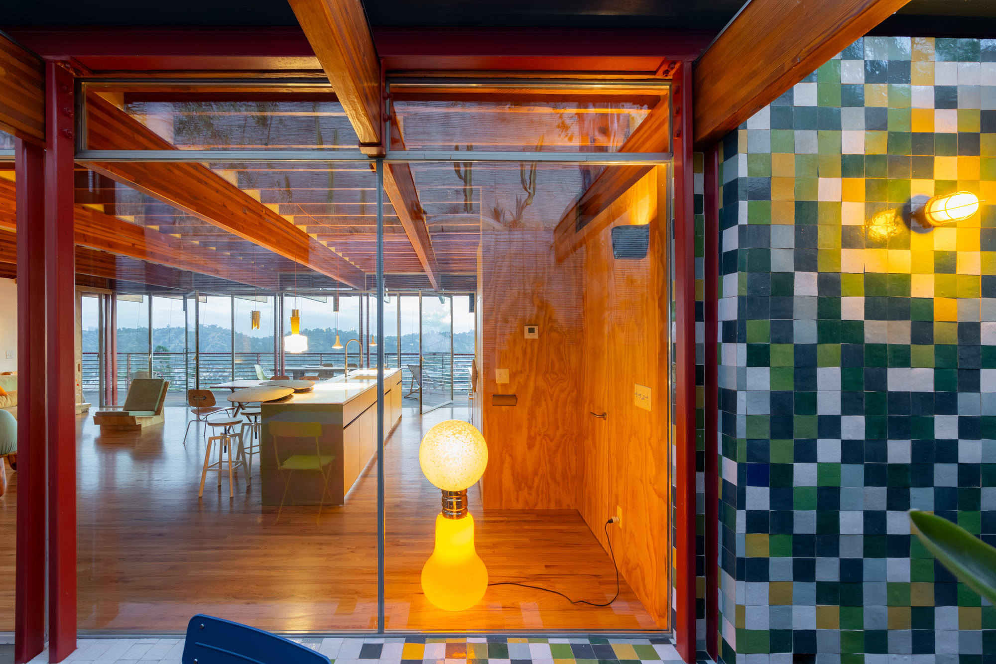 Glass doorway framed by timber beams with chequered tile wall and yellow floor lamp