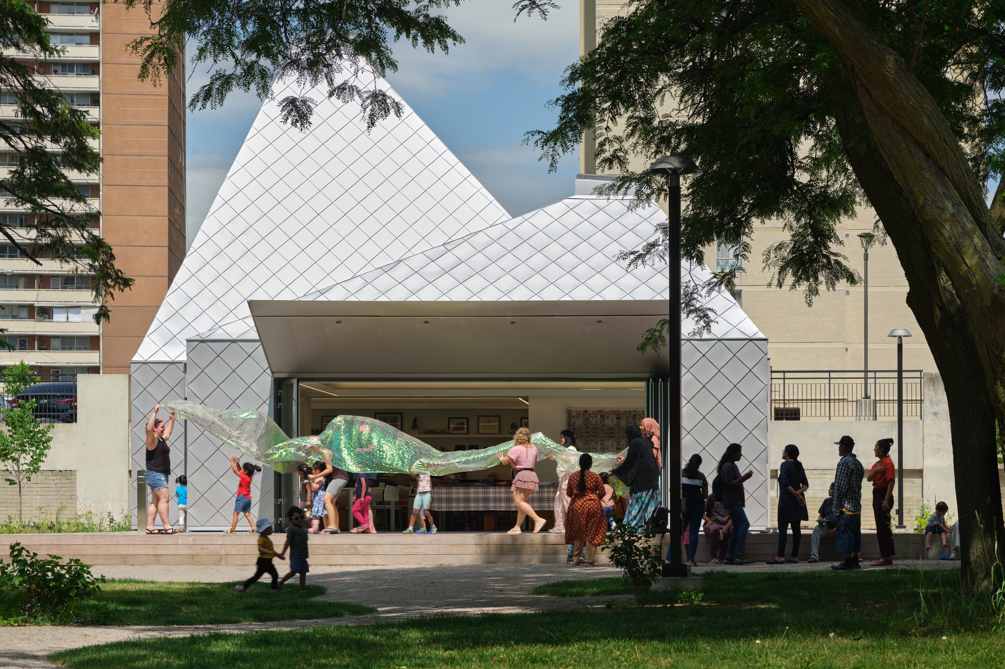 Front elevation of the open pavilion with deep overhang sheltering visitors beneath tree shade