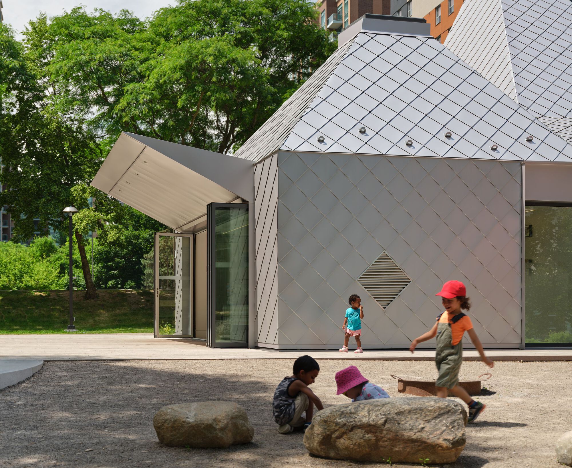 Side facade showing the folding glass doors and diamond vent detail with children playing on boulders