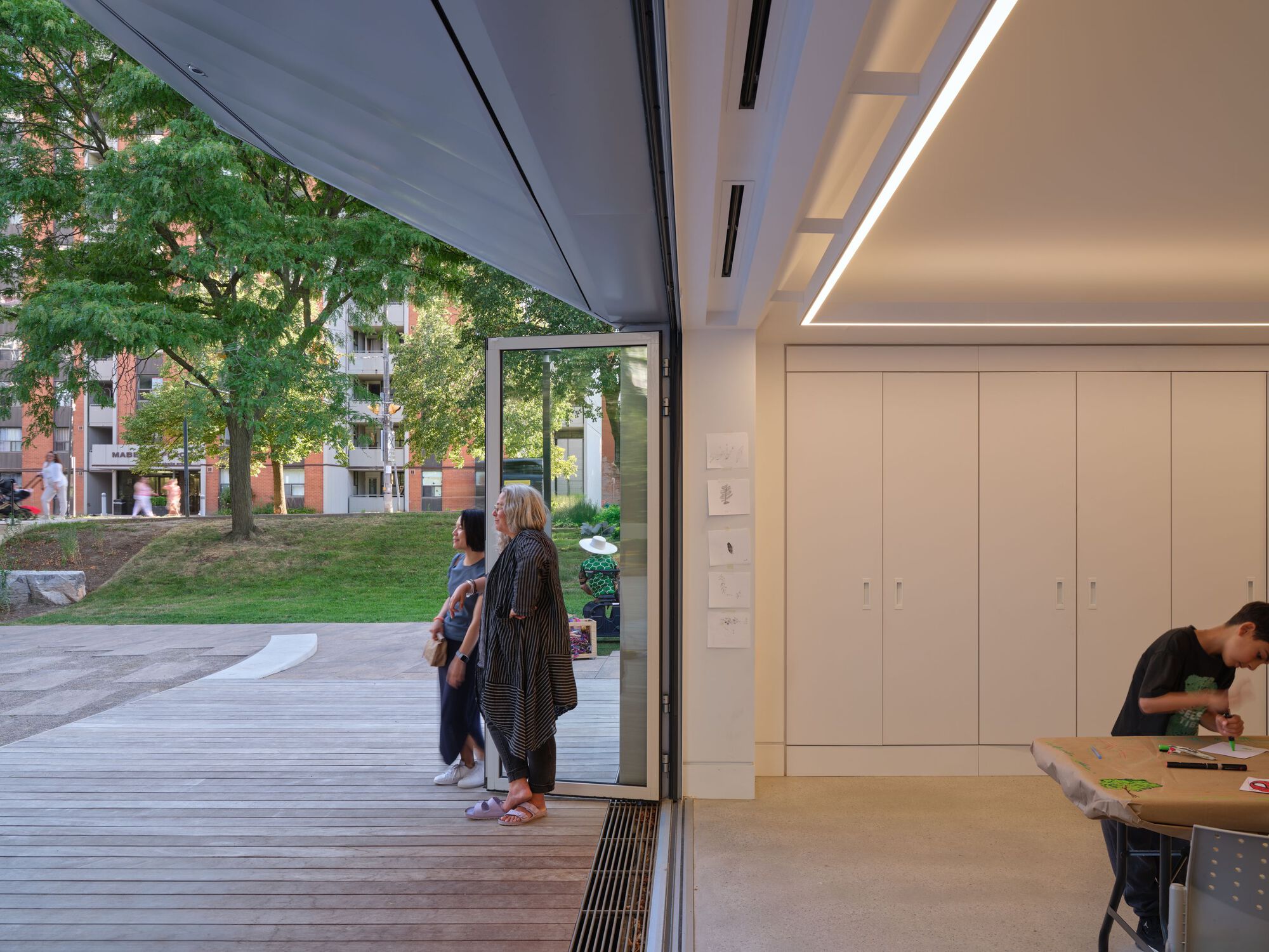 Interior space with floor-to-ceiling glass sliding doors opening to a timber deck and park beyond