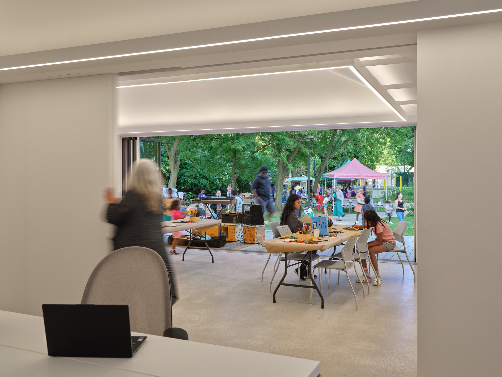 View through interior workspace showing recessed lighting coves and community activities on the outdoor deck