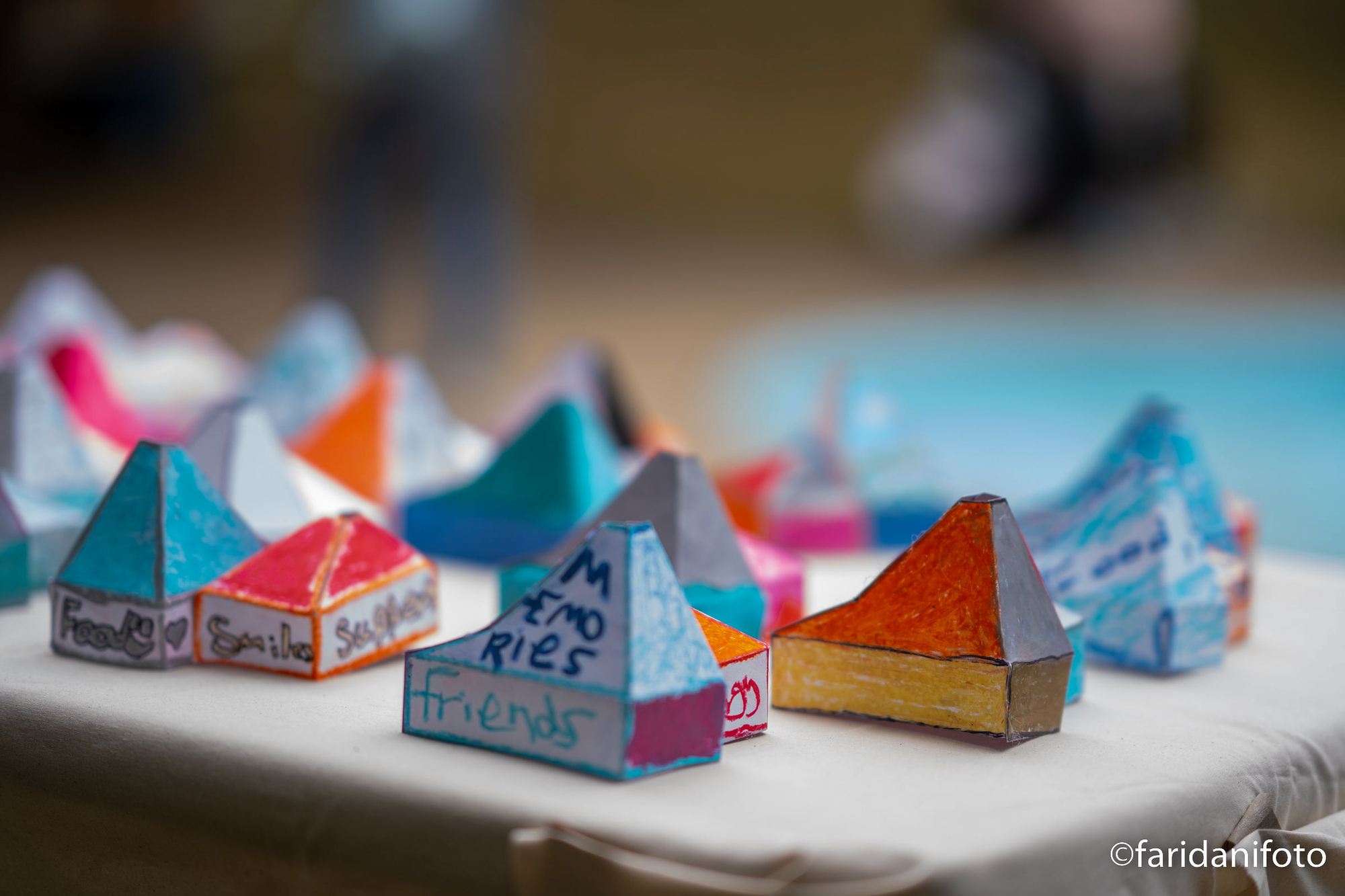 Colorful paper models with pyramidal roofs arranged on a white surface with handwritten labels