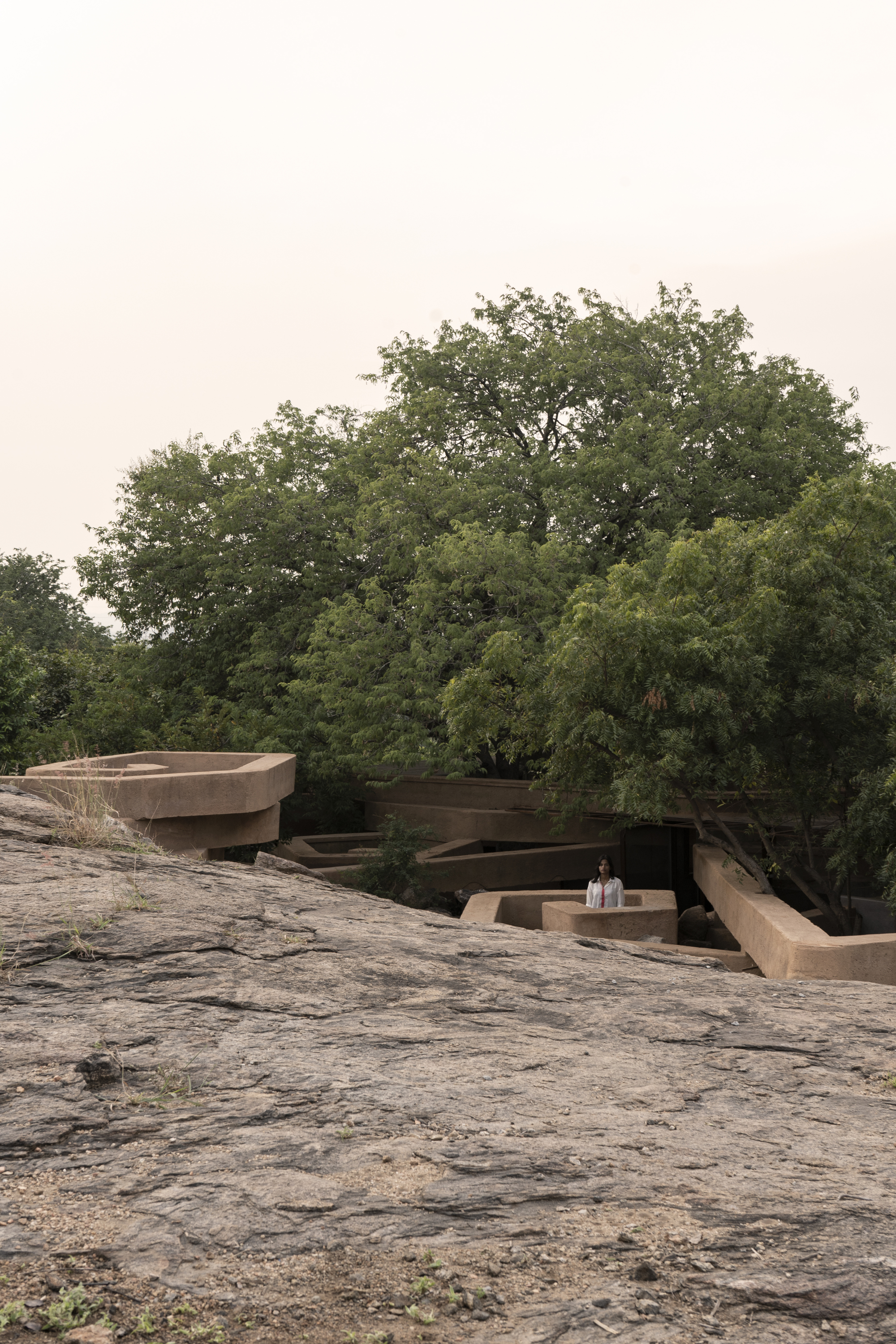 Two figures on the rocky landscape beside the layered rammed earth volumes nestled among mature trees