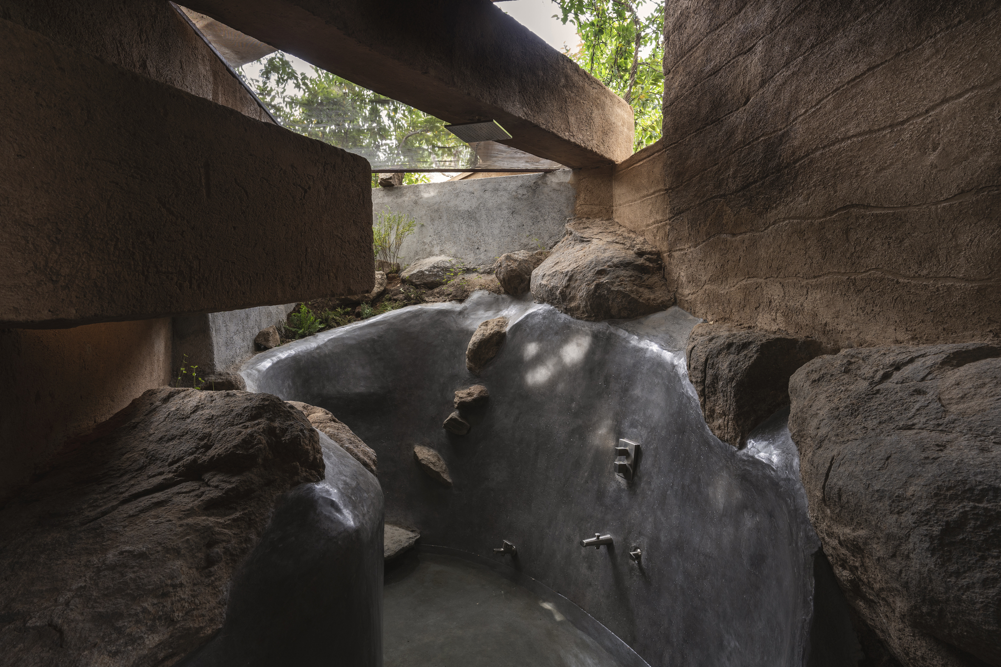 Sunken bathing pool carved into natural rock beneath concrete cantilevers and dappled light