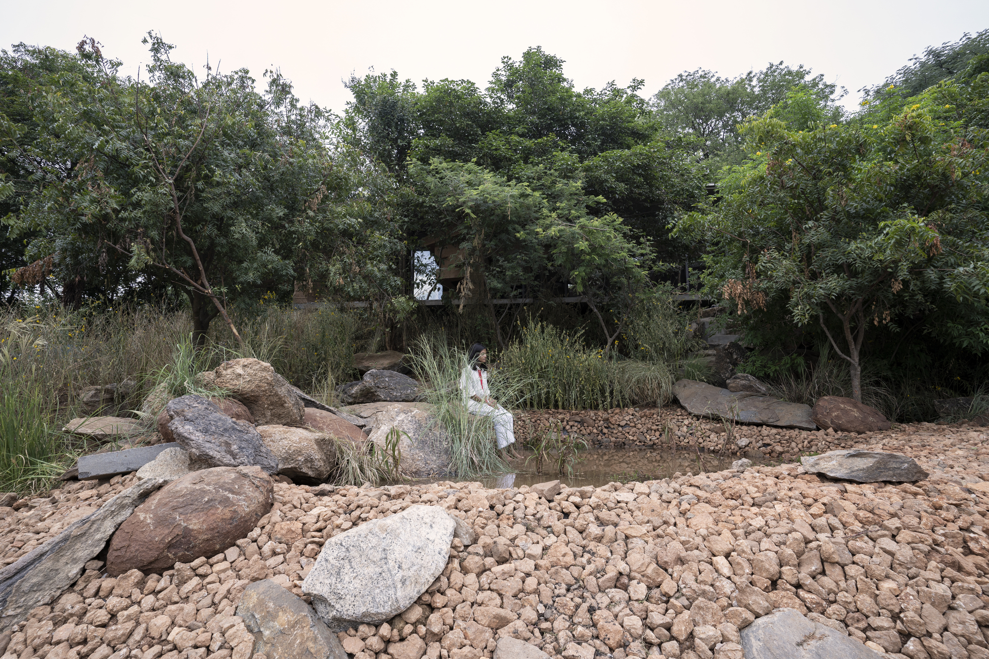 Natural pond surrounded by boulders and pebble beach with a figure wading in shallow water