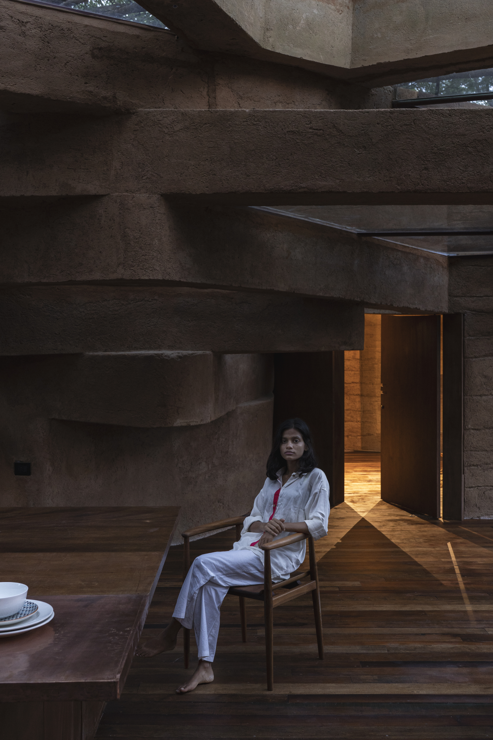 Layered earthen walls and timber flooring with a seated figure illuminated by warm afternoon light
