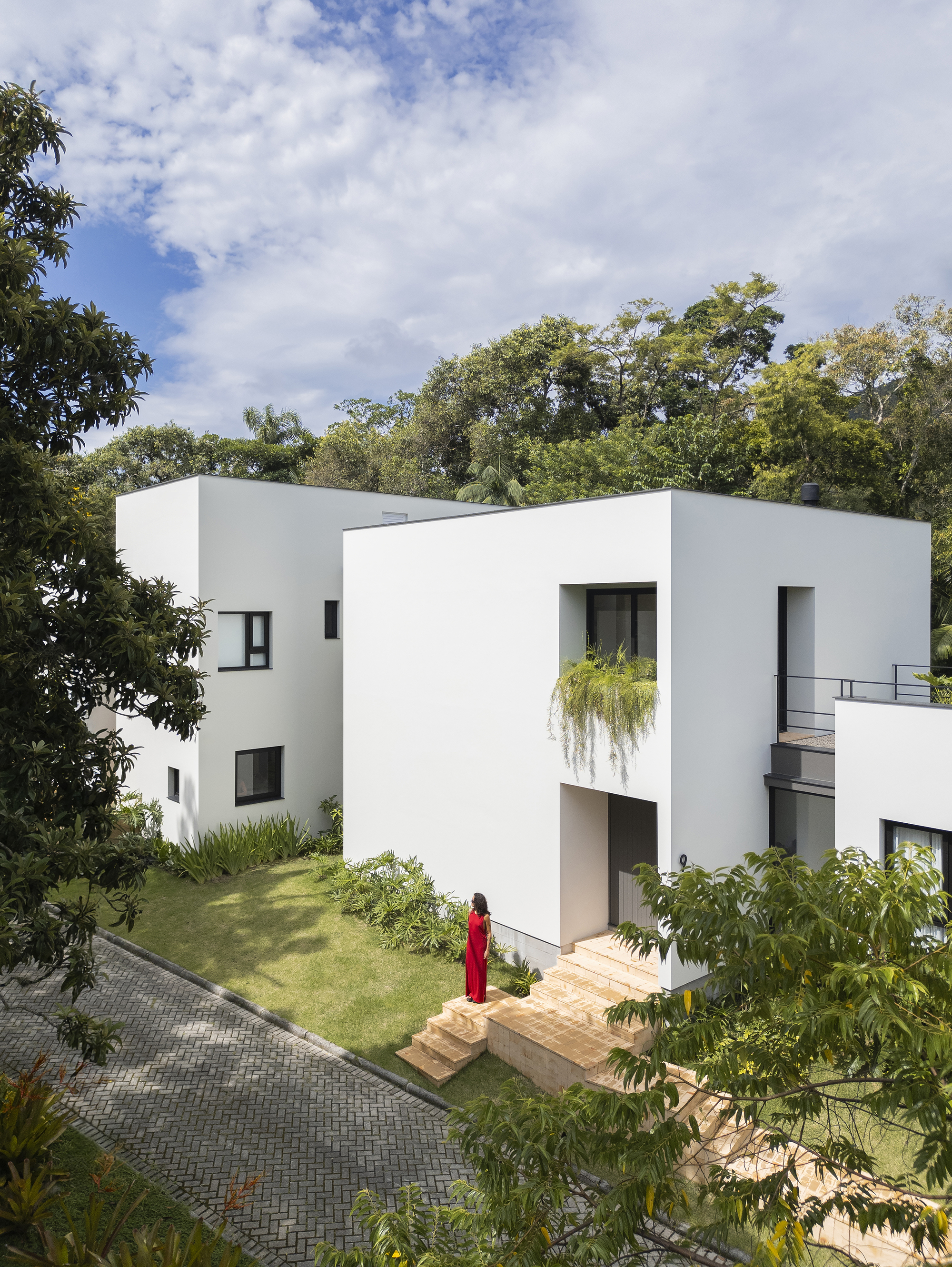 Elevated white facade with recessed entrance and figure in red descending brick steps to lawn