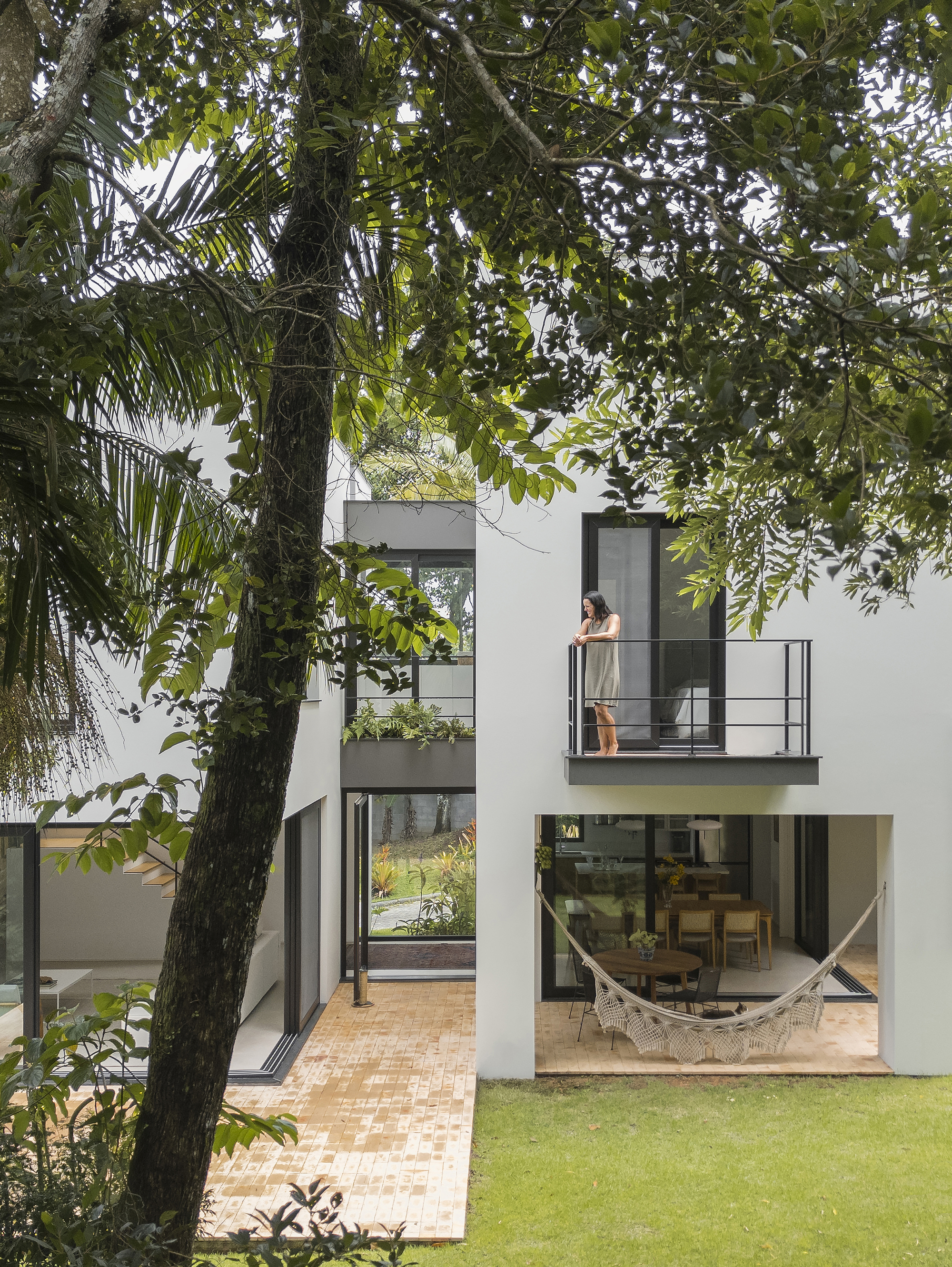 Cantilevered balcony with steel railing and figure seen through trees next to glazed living space