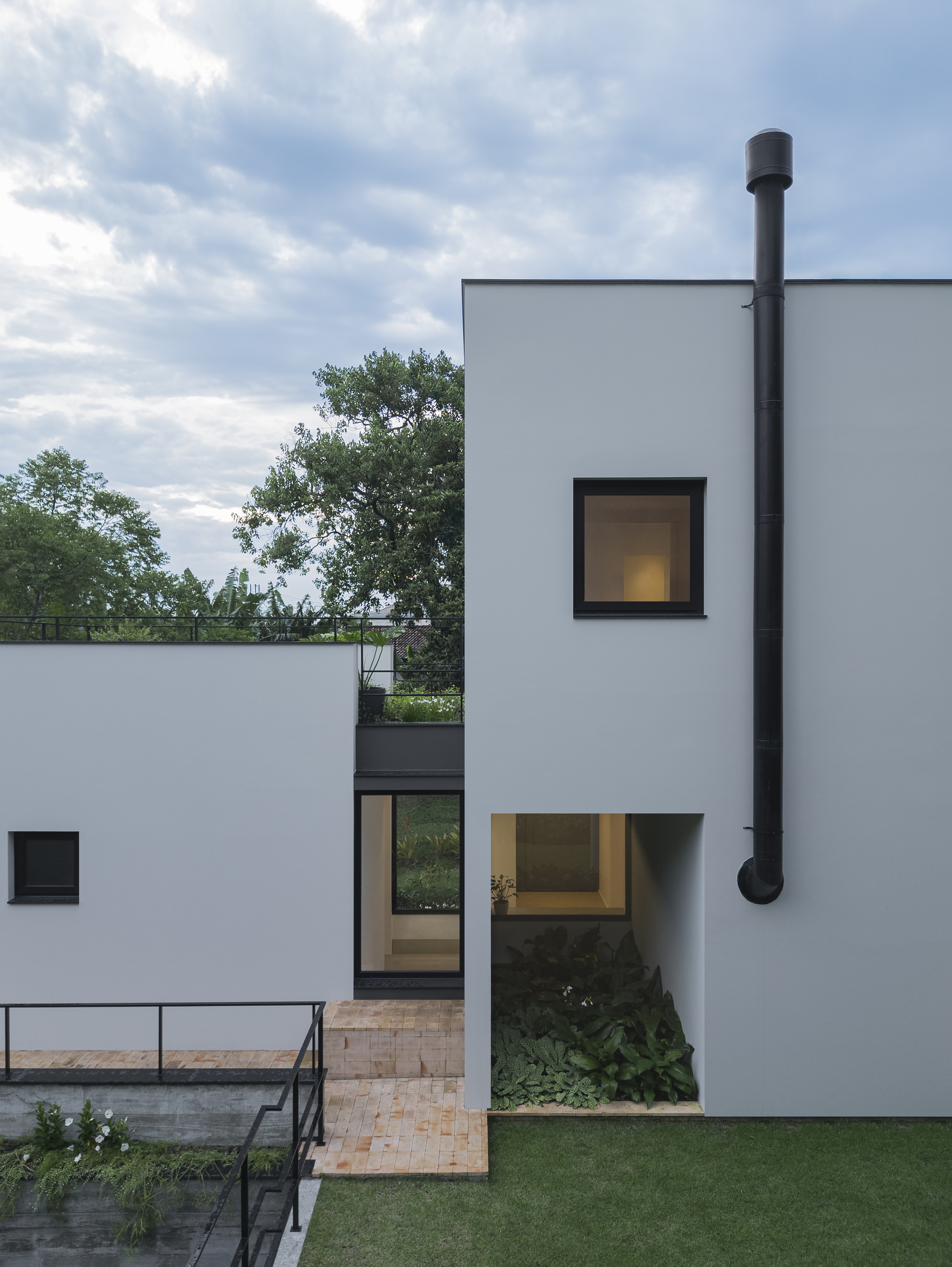 External black metal chimney flue rising along the white facade above recessed glazed entry
