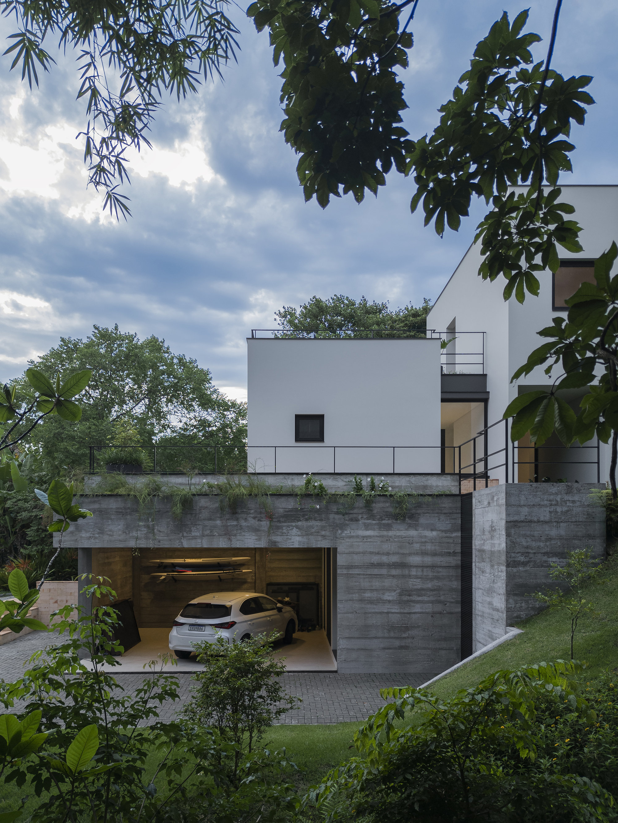 Board-formed concrete garage base with open door revealing parked car beneath white upper volume