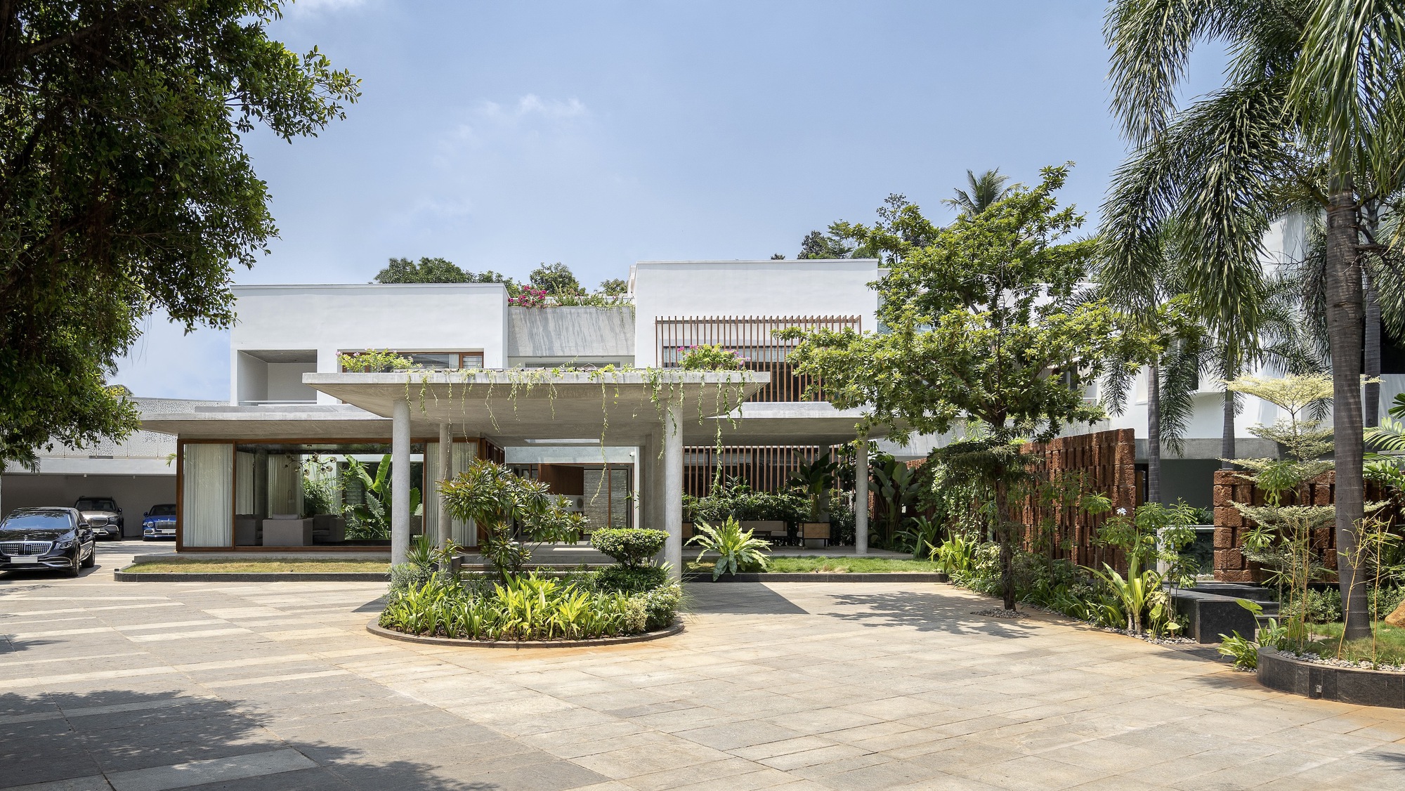 Entry driveway view showing white concrete canopy, timber screens, and circular planted island