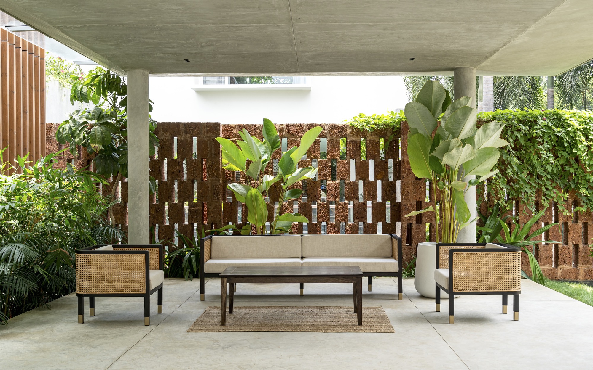 Covered terrace with cane furniture facing a patterned red block screen wall and tropical plantings