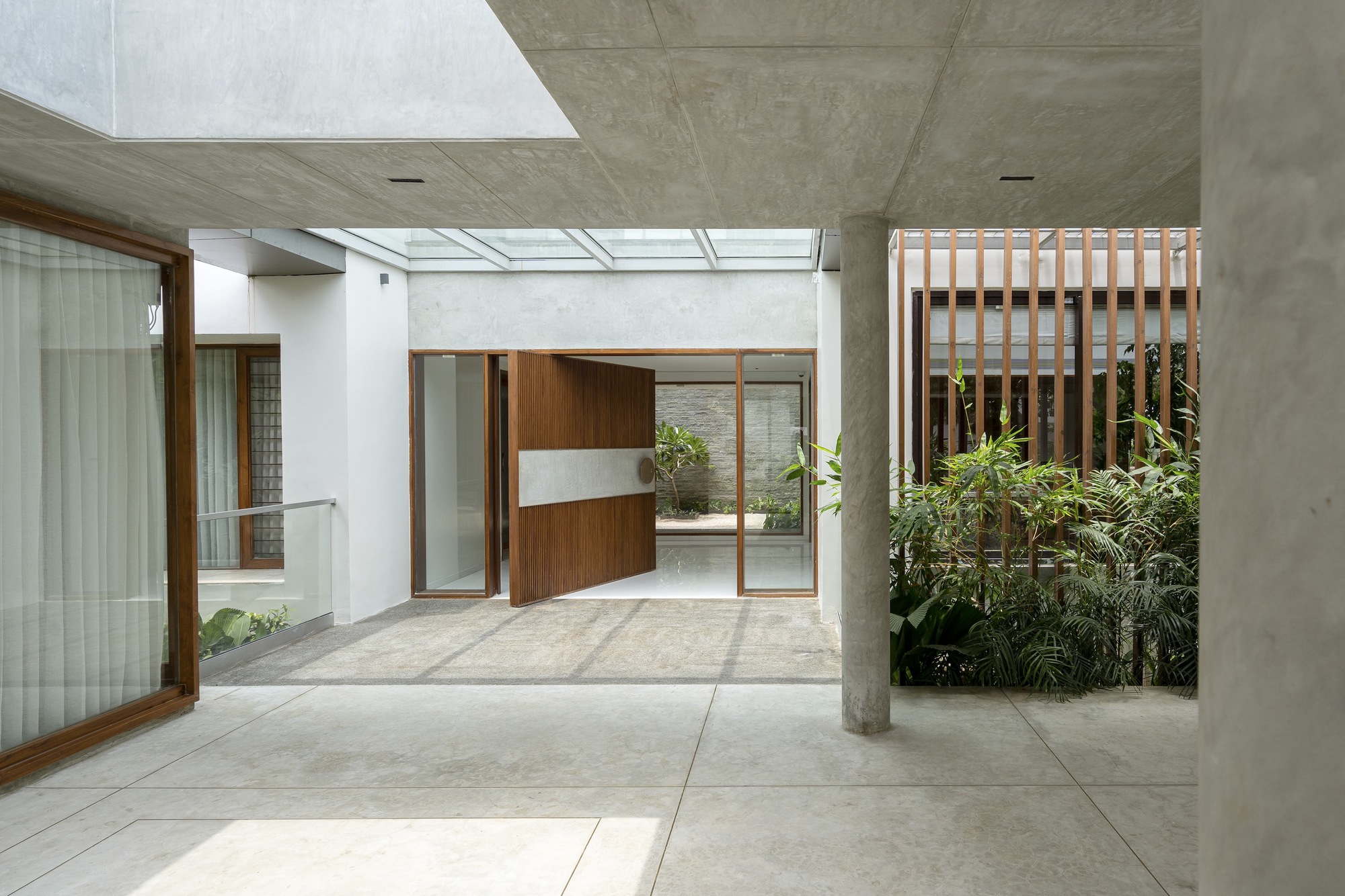 Concrete portico with cylindrical column framing the timber pivot door and skylights above the entrance