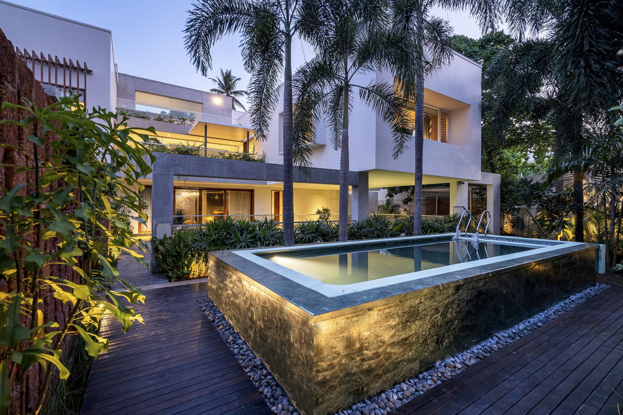 Elevated lap pool with textured stone base and underwater lighting surrounded by timber deck and palms at twilight