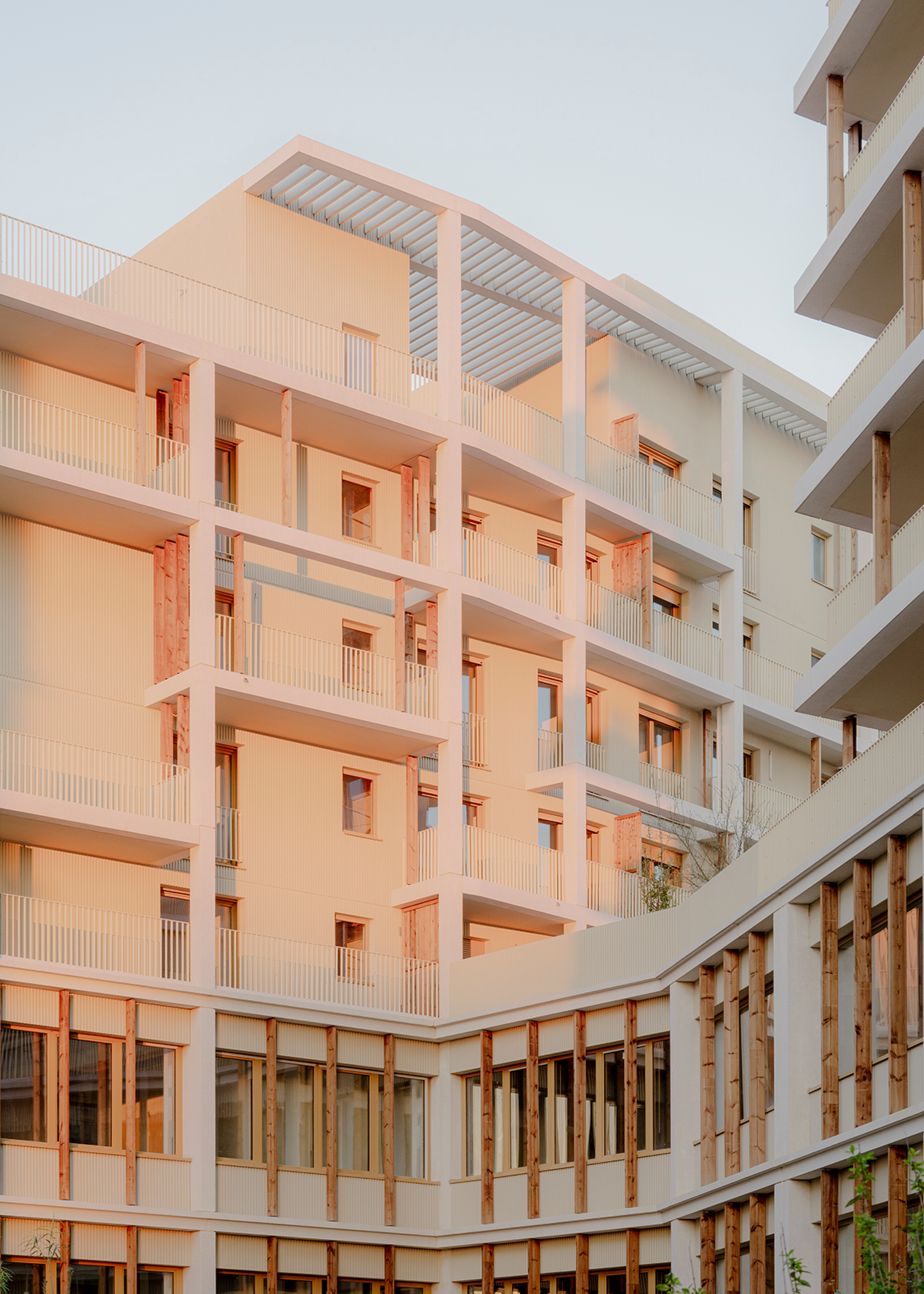 Multi-story courtyard elevation with white balconies and timber-framed openings in warm evening light