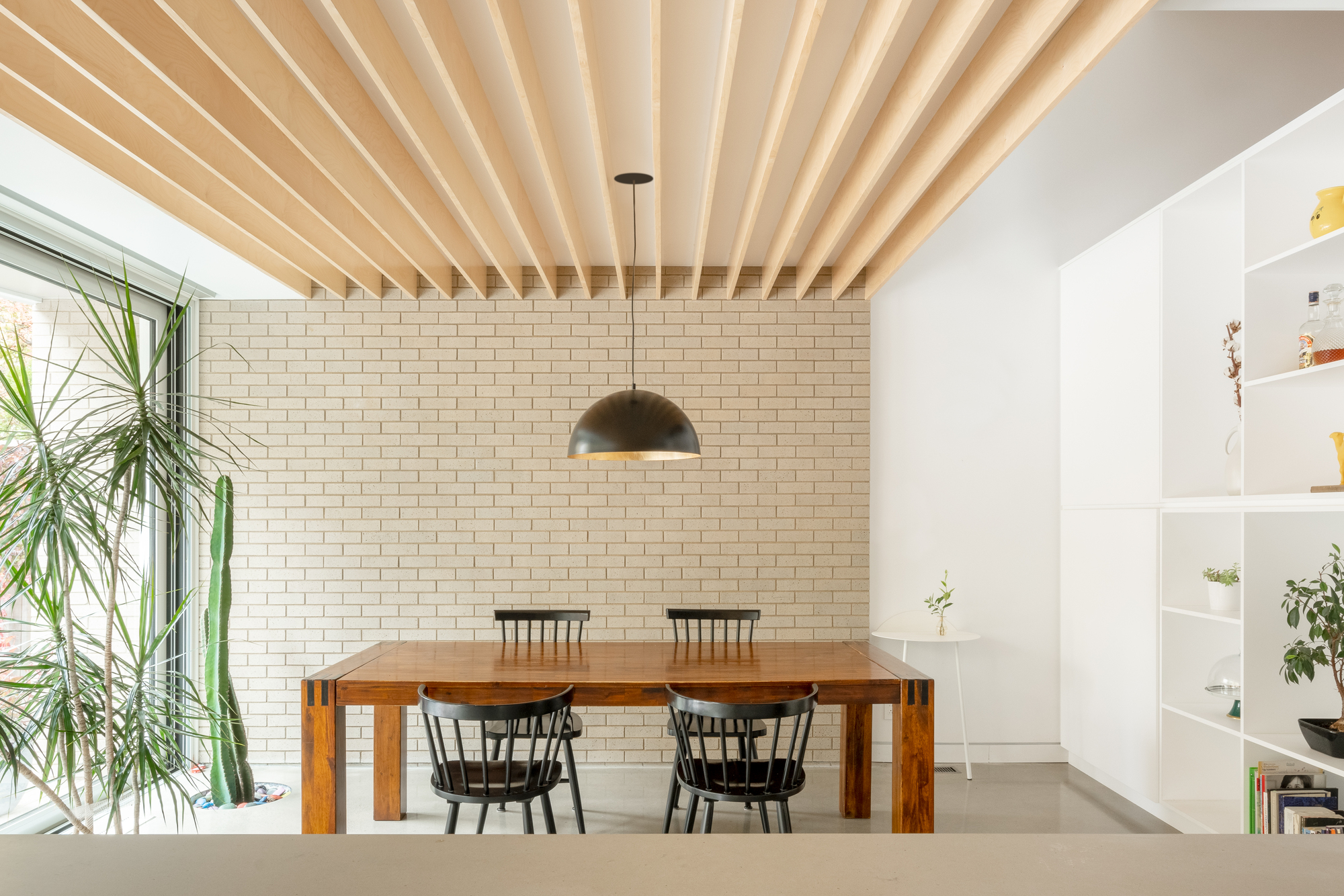 Dining room with exposed timber beam ceiling and cream brick wall beside a window with plants