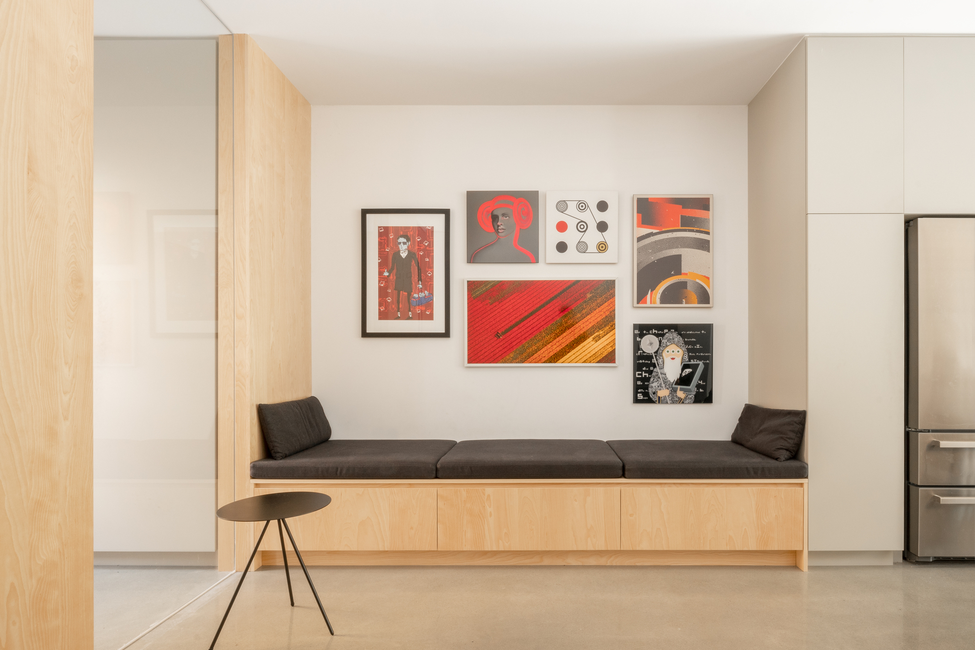 Built-in bench with cushions beneath a gallery wall of framed prints in red tones
