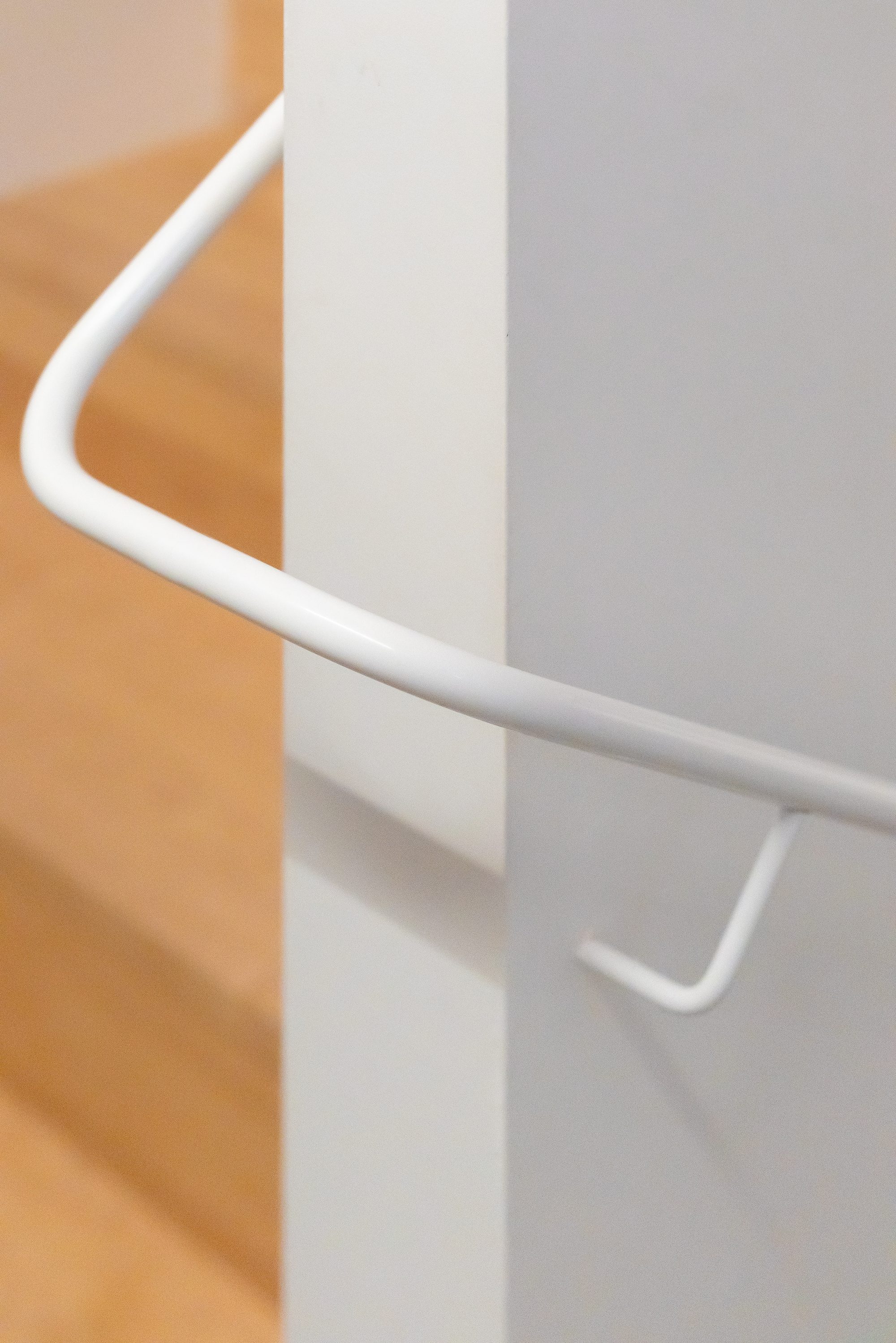 Detail of a white tubular metal handrail mounted on a white wall beside yellow tiled surfaces