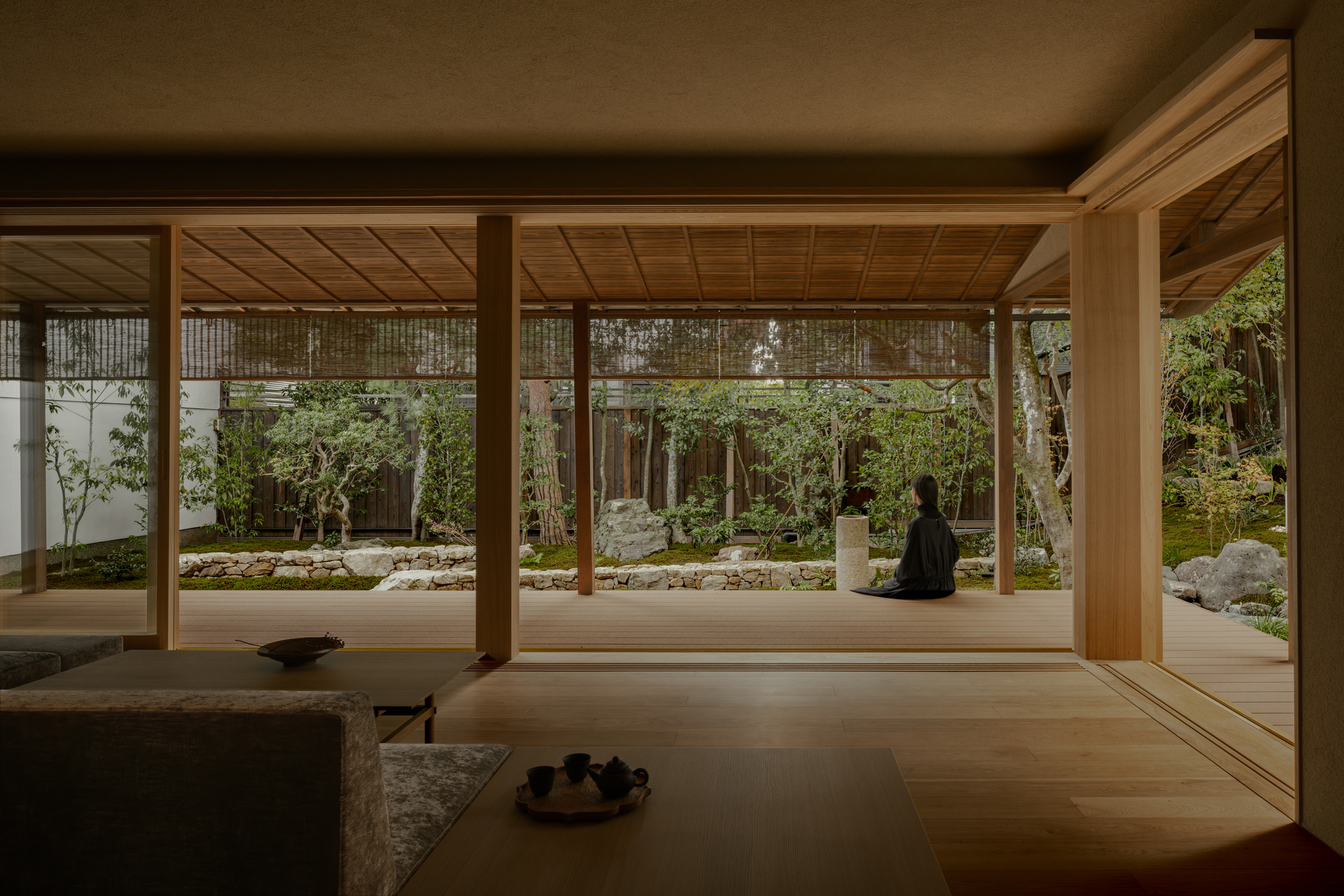 Timber-framed pavilion opening onto a rock garden with moss, stones, and a seated Buddha sculpture
