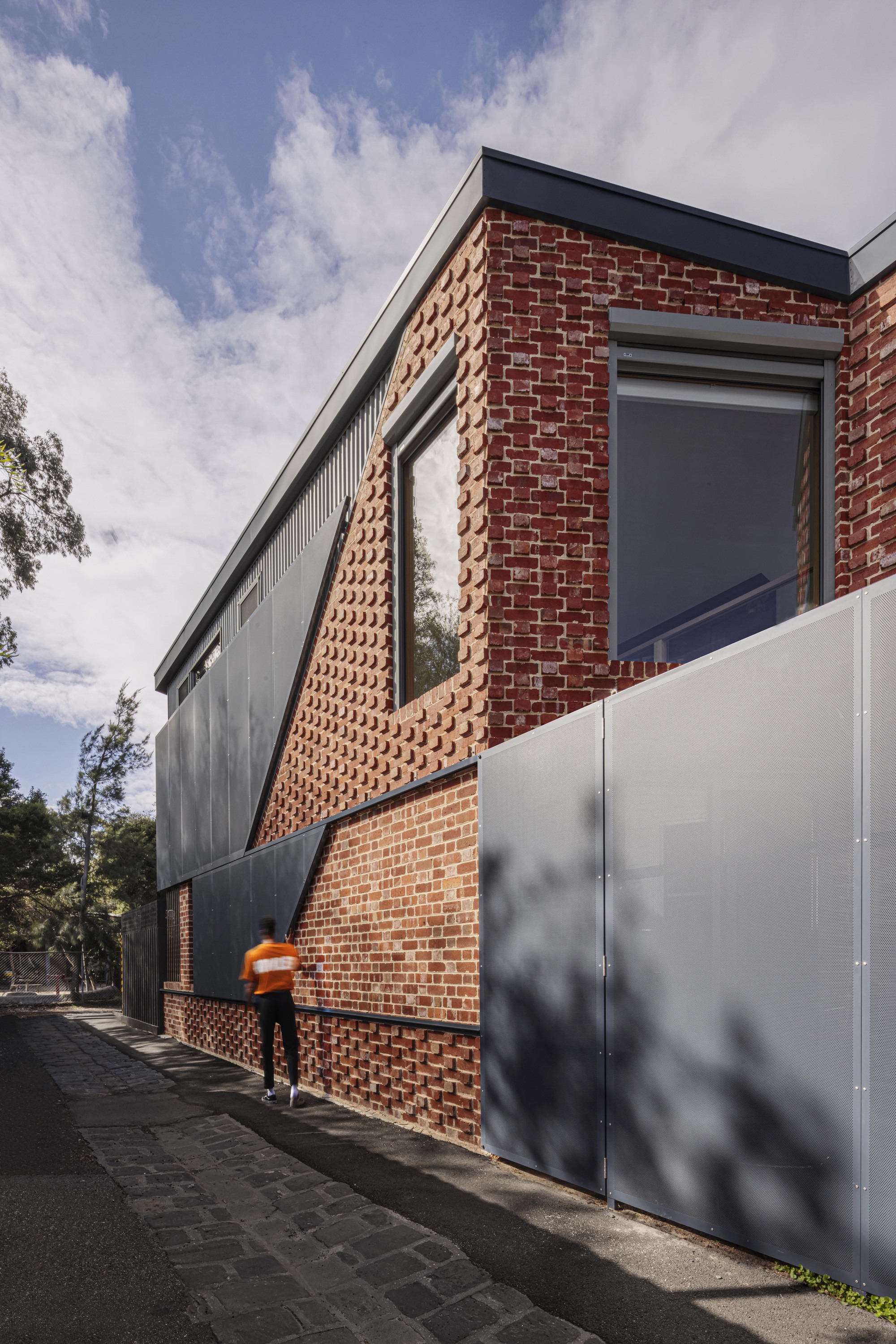 Street view of the two-story facade with perforated brick panels and metal cladding under afternoon shadows