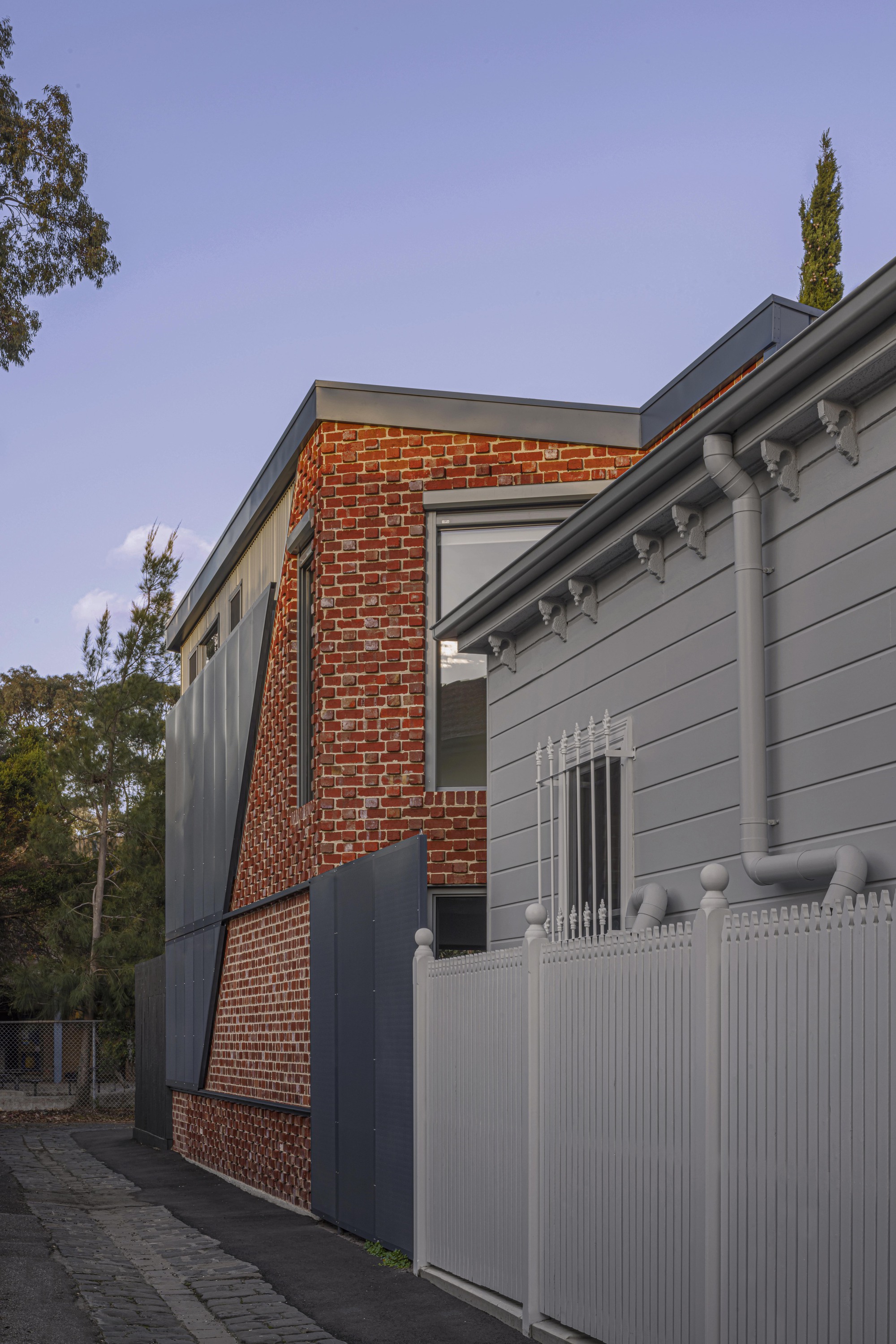 Street view of the brick and weatherboard facade with white picket fence at dusk
