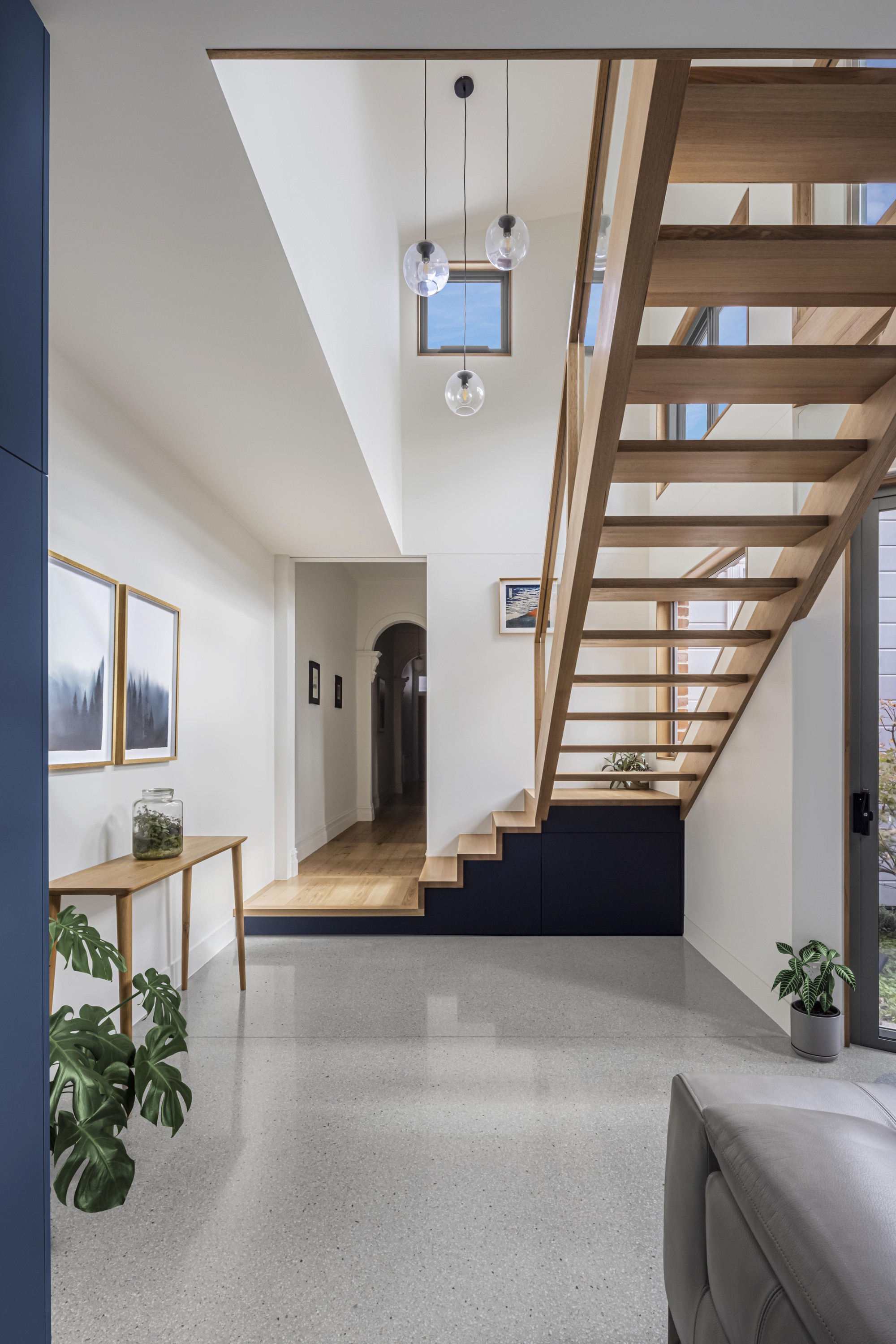 Entry hall with timber open-tread staircase and pendant globe lights beside potted plants
