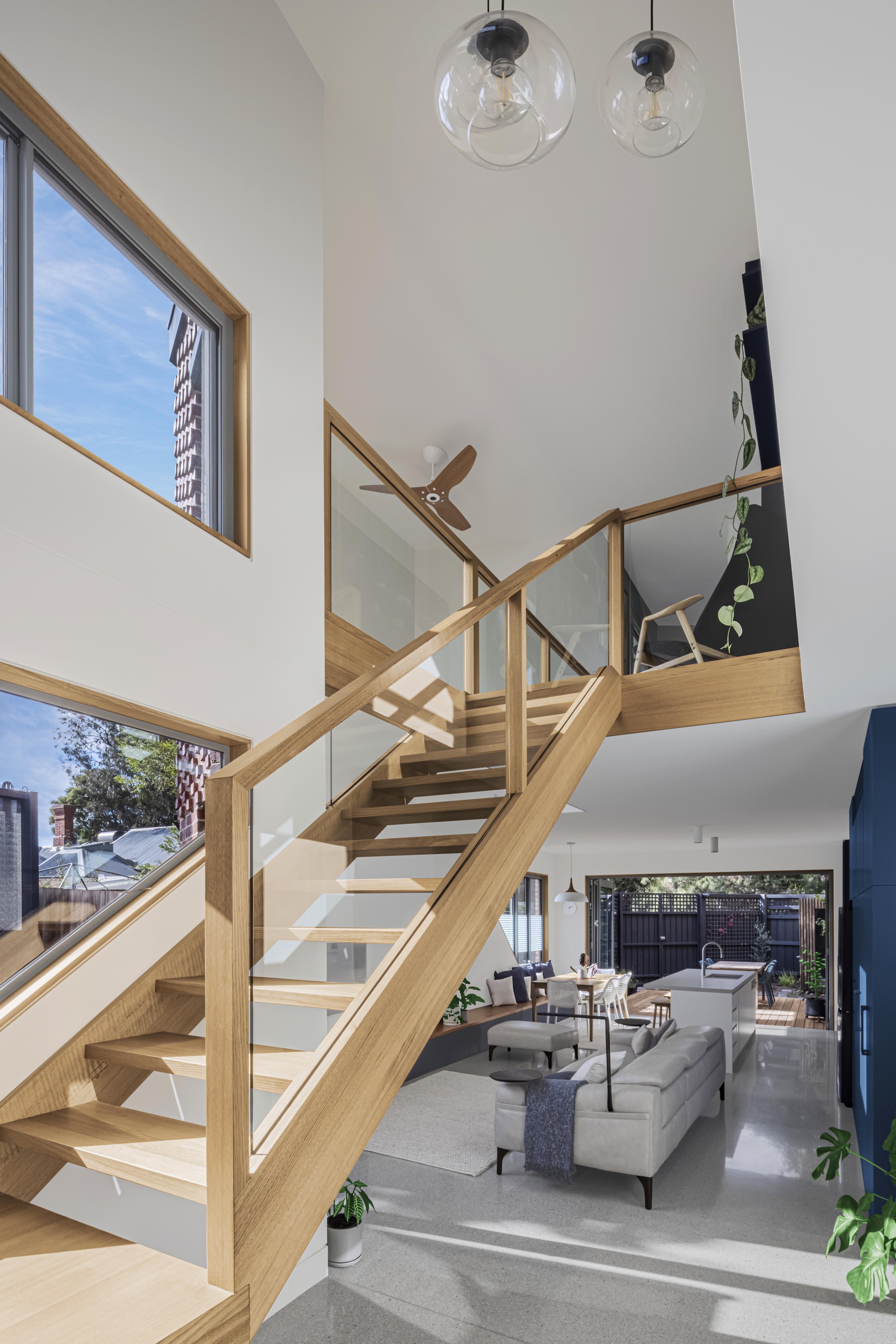 Double-height living space with timber and glass staircase overlooking the open-plan interior