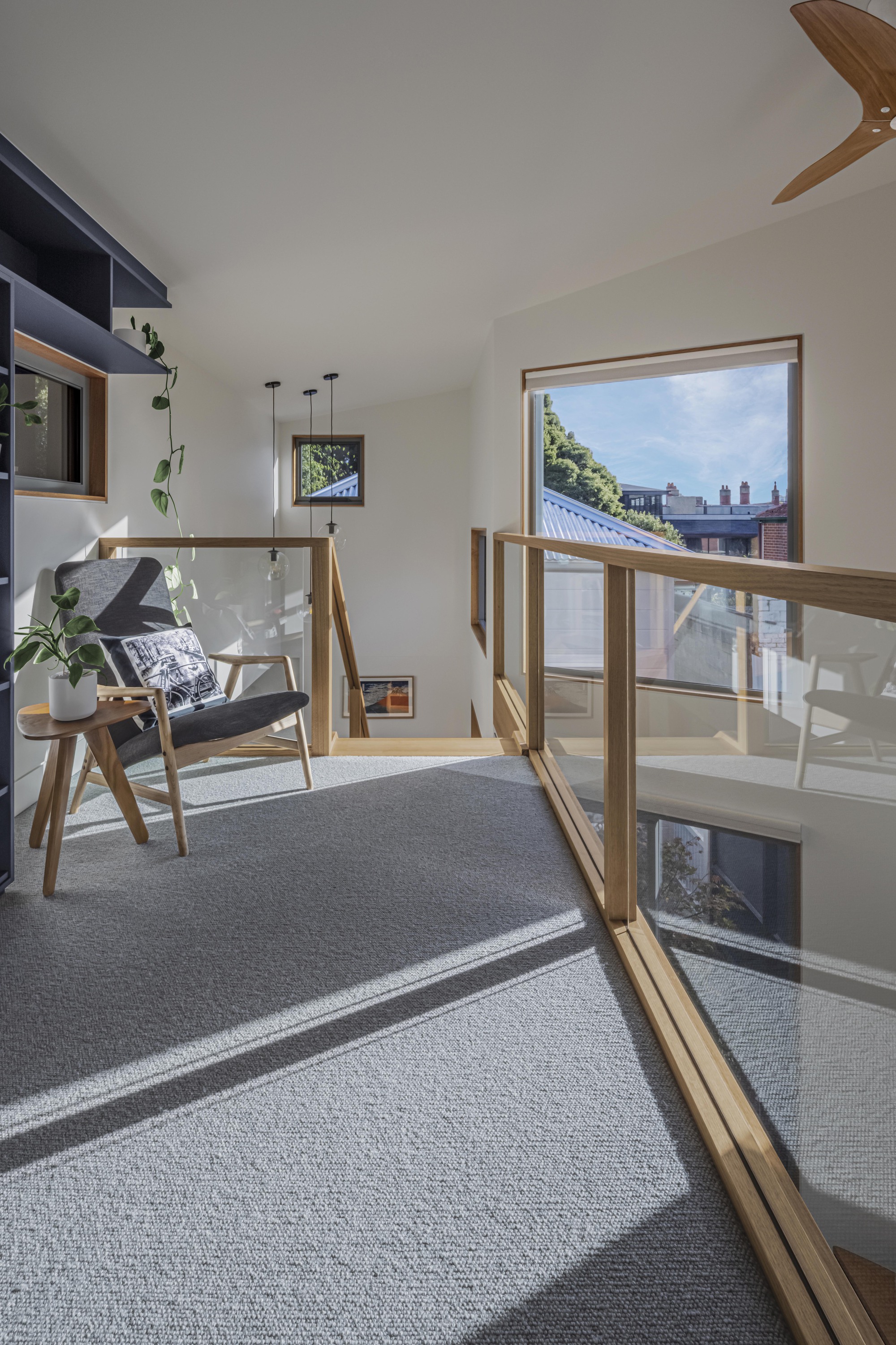 Upper-level void with timber balustrade and armchair bathed in afternoon sunlight