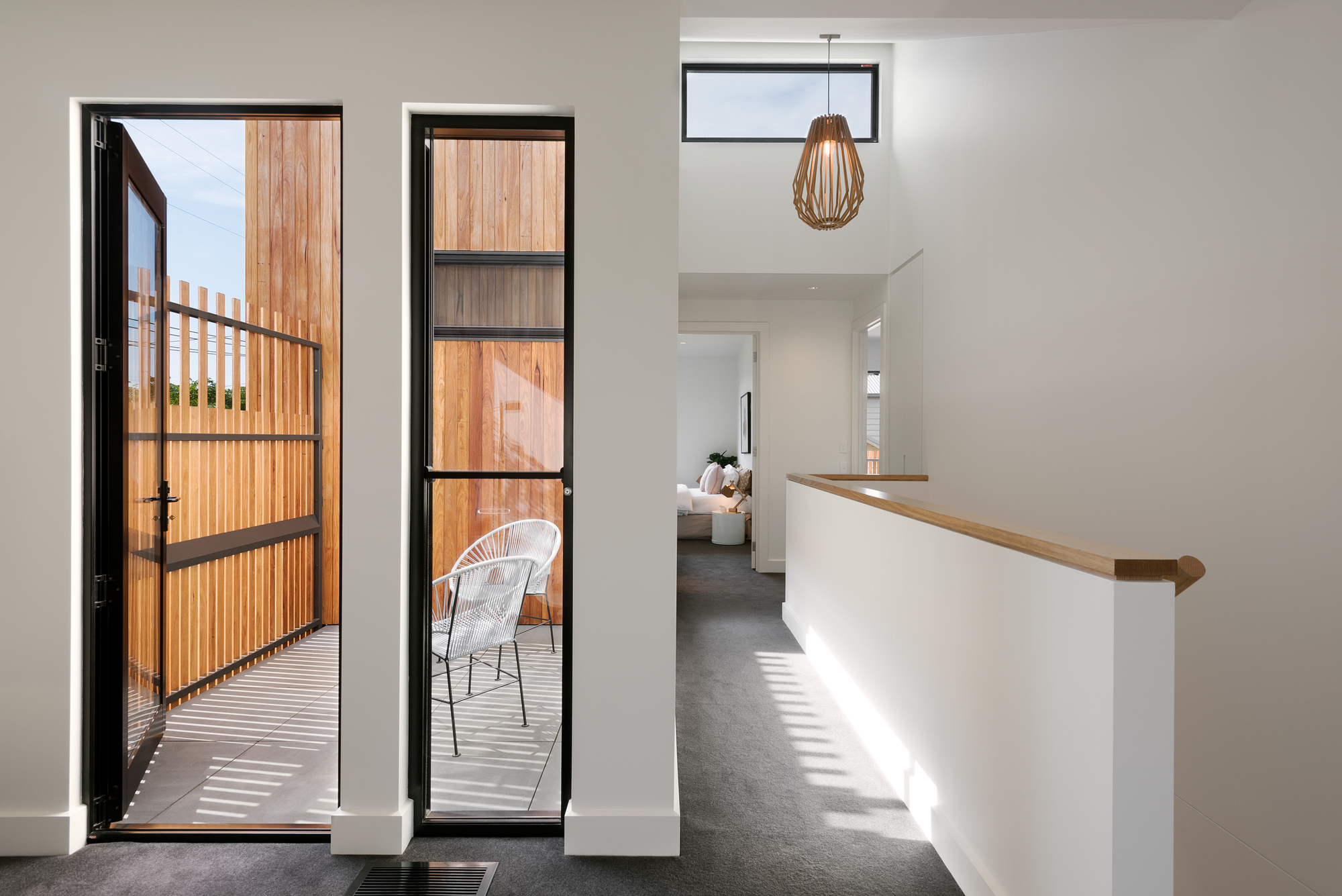 Upper landing with timber-capped balustrade and black-framed doors opening to a timber-screened balcony in afternoon light