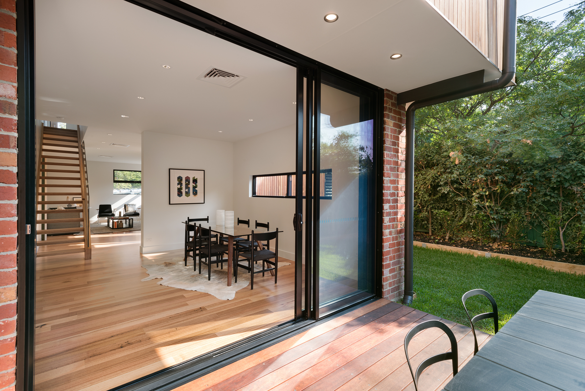 Open sliding glass doors connecting dining room with timber floor to rear lawn