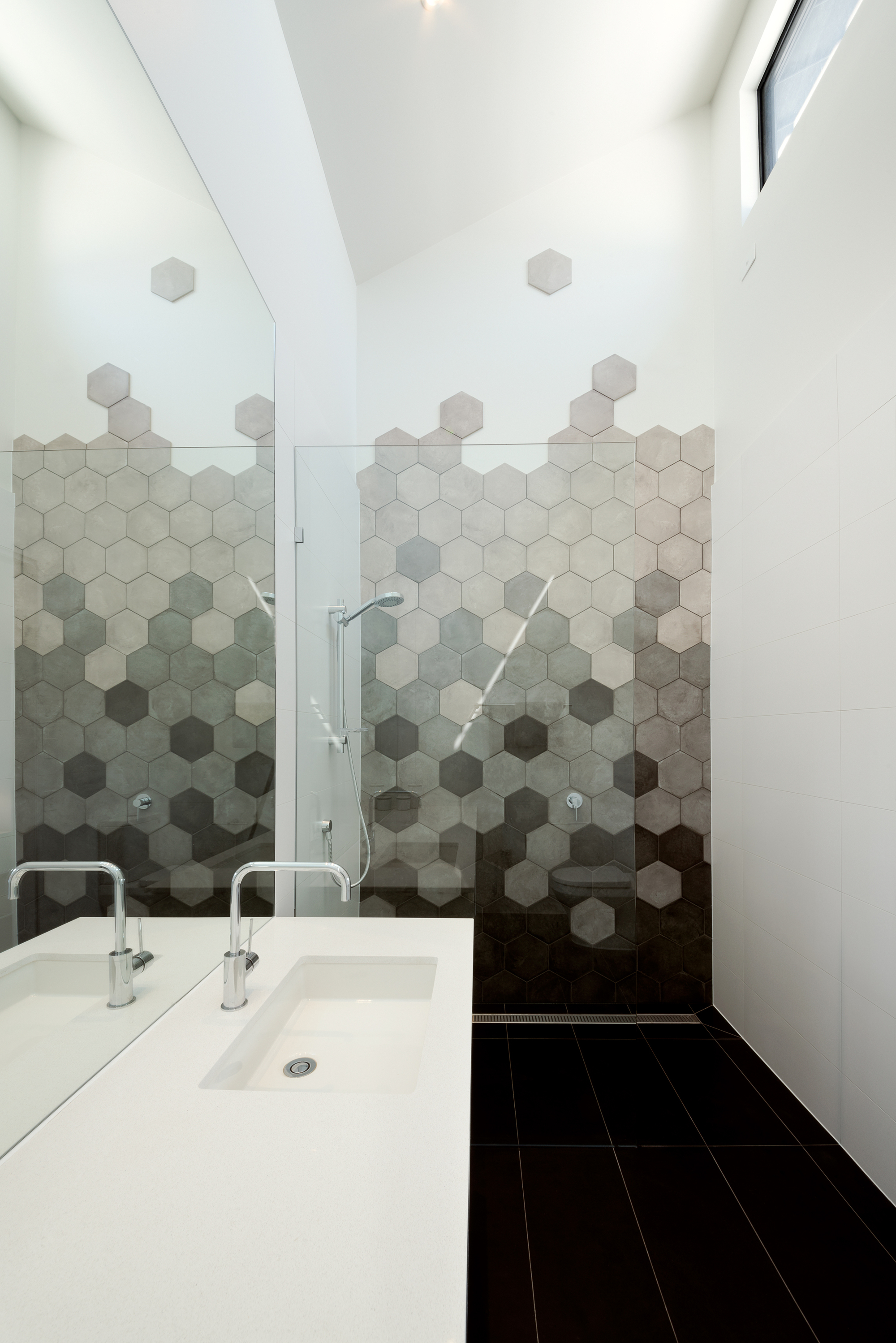 Bathroom with hexagonal tile gradient wall transitioning from light to dark beneath a skylight