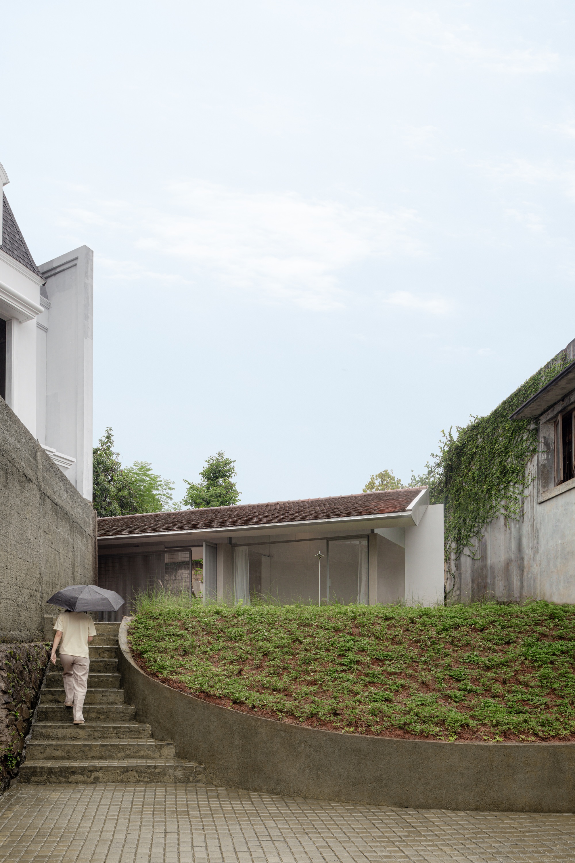 Person with umbrella ascending concrete steps beside the planted green roof under overcast sky