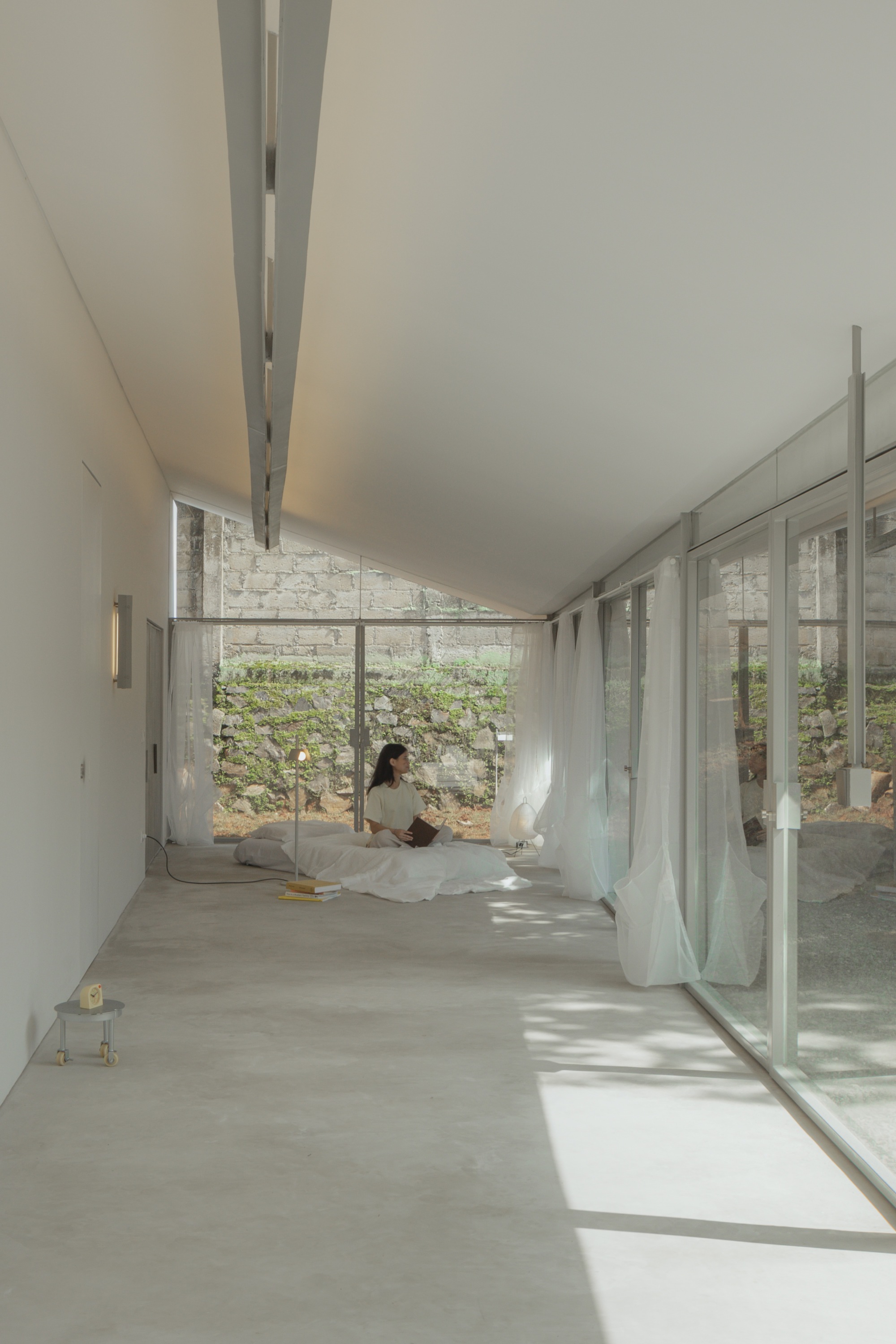 Interior hallway with full-height glazing overlooking a planted courtyard with a seated occupant inside