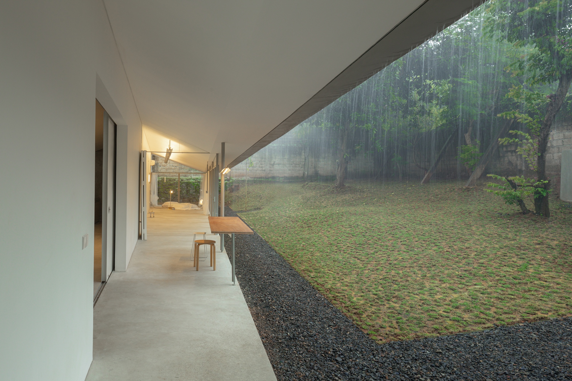 Covered exterior corridor with concrete floor looking toward the garden through columns of rain