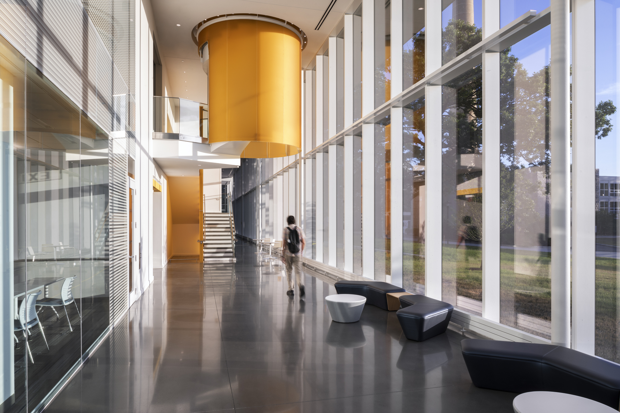 Double-height lobby with cylindrical yellow volume and polished concrete floor as figure walks past angular seating