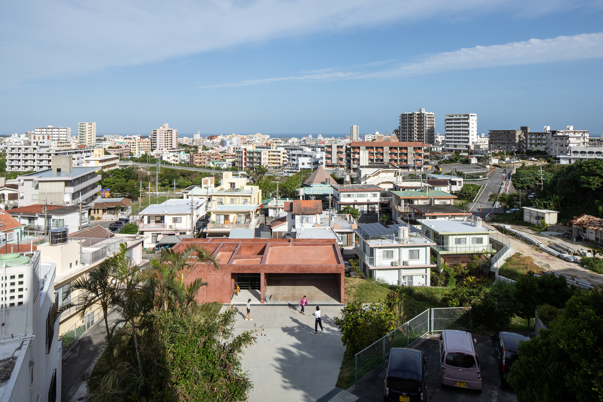 Elevated view of the rammed earth roof among neighborhood houses and apartment blocks under bright sky