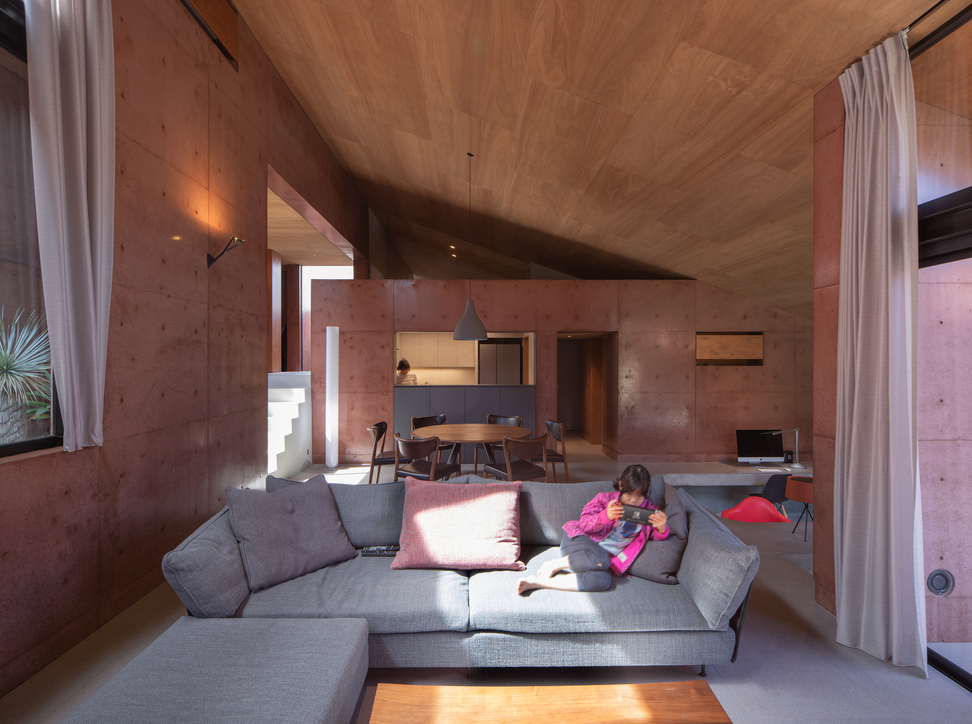 Living space with folded plywood ceiling and diagonal sunlight across a grey sofa