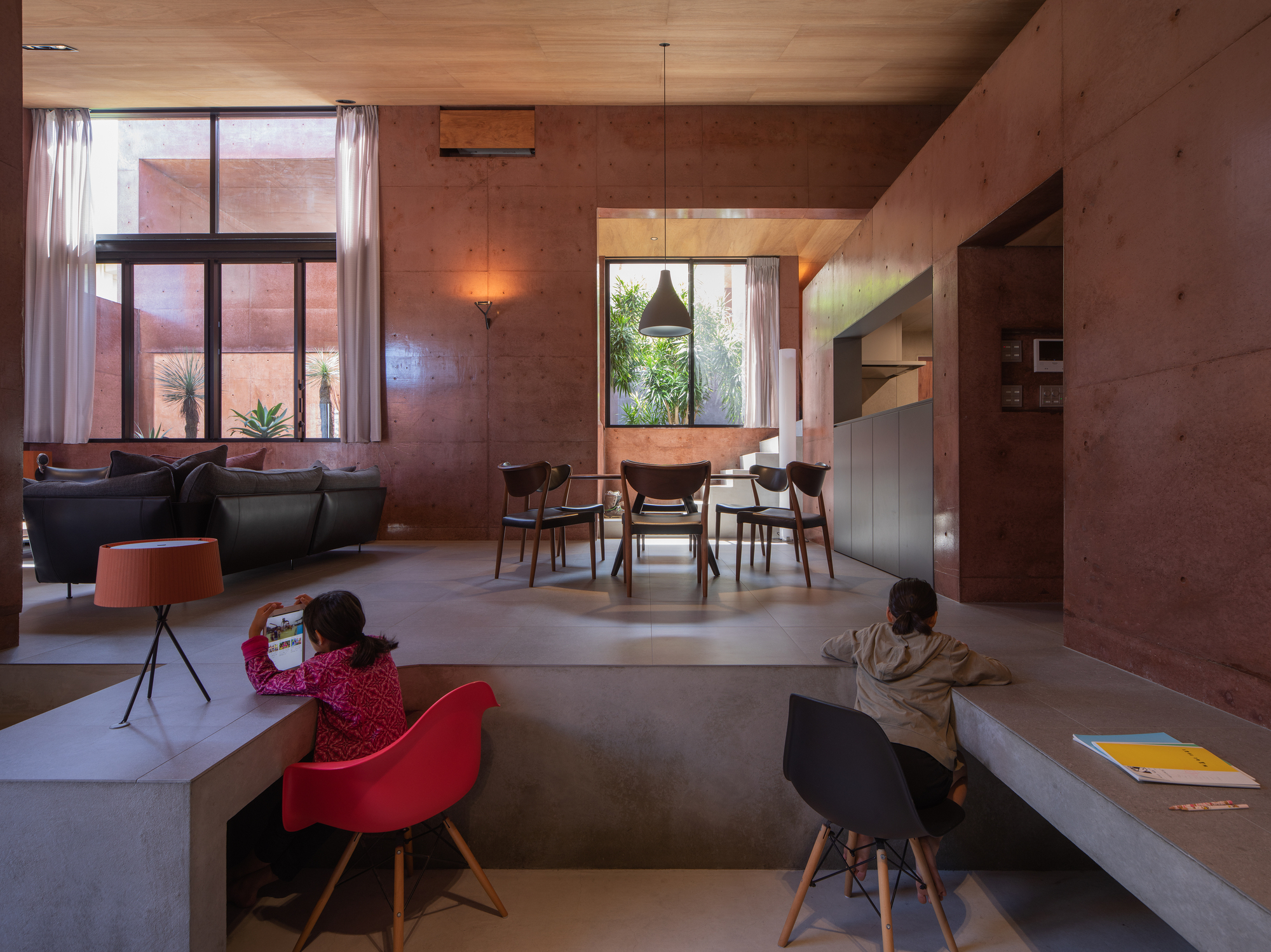 Open living and dining space with rammed earth walls and children playing at dusk